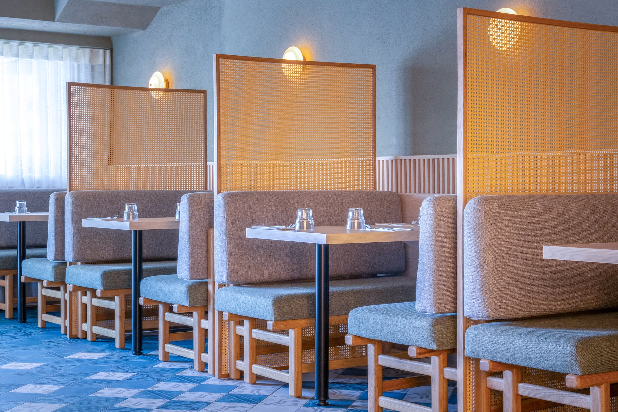Modern restaurant interior with grey booths and cane privacy screens.