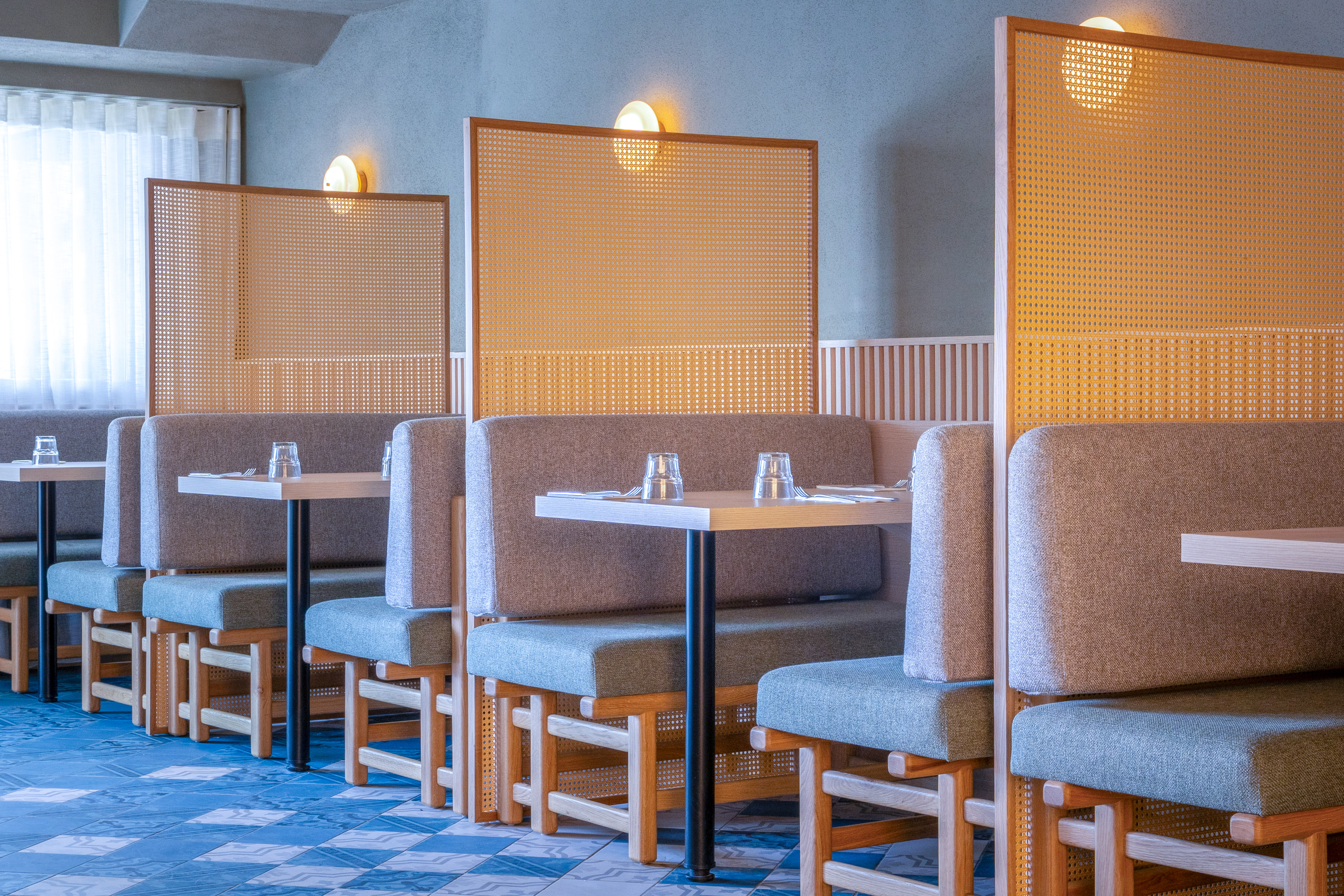 Modern restaurant interior with grey booths and cane privacy screens.