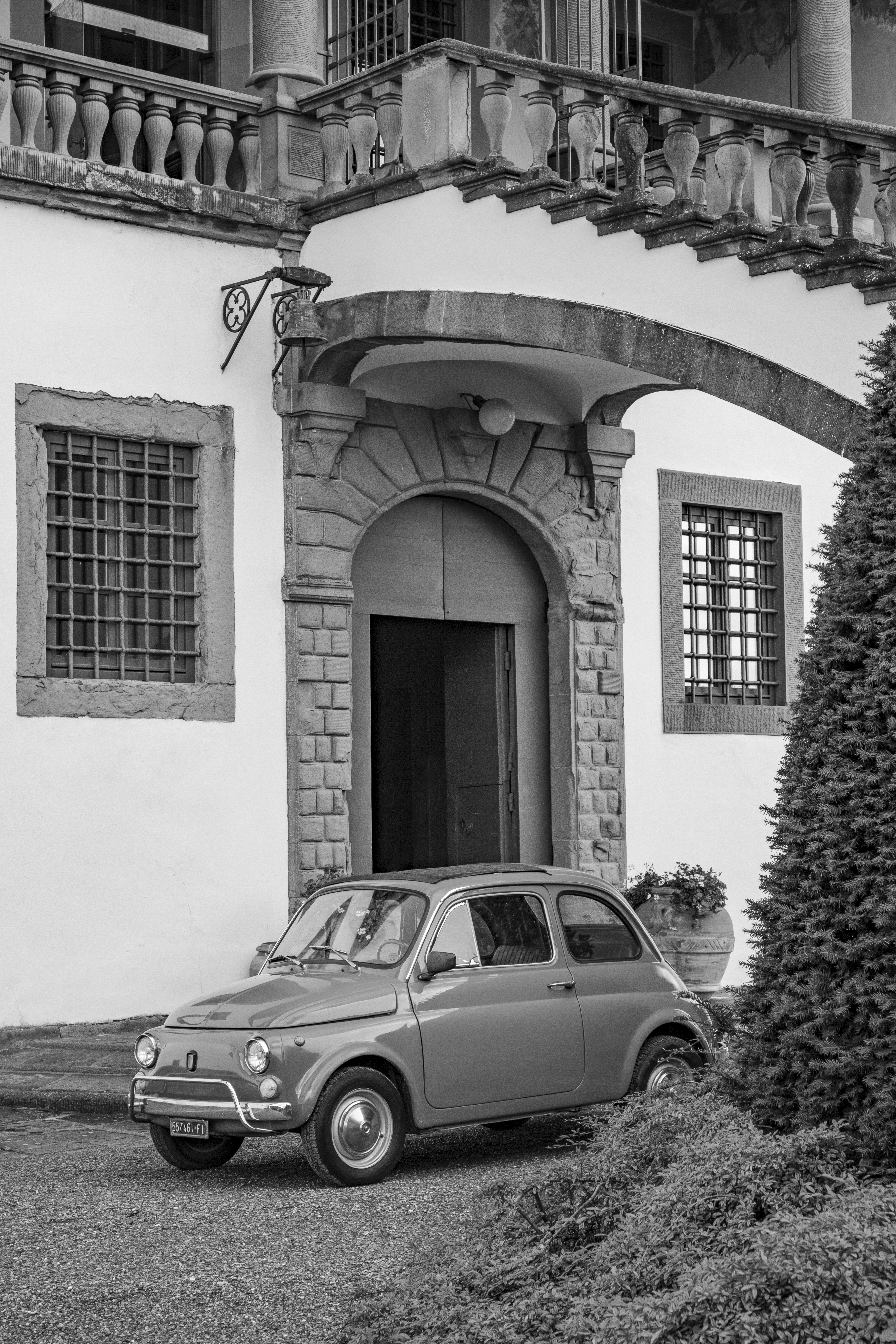 B&W vintage Fiat 500 parked at a historic Italian villa entrance.