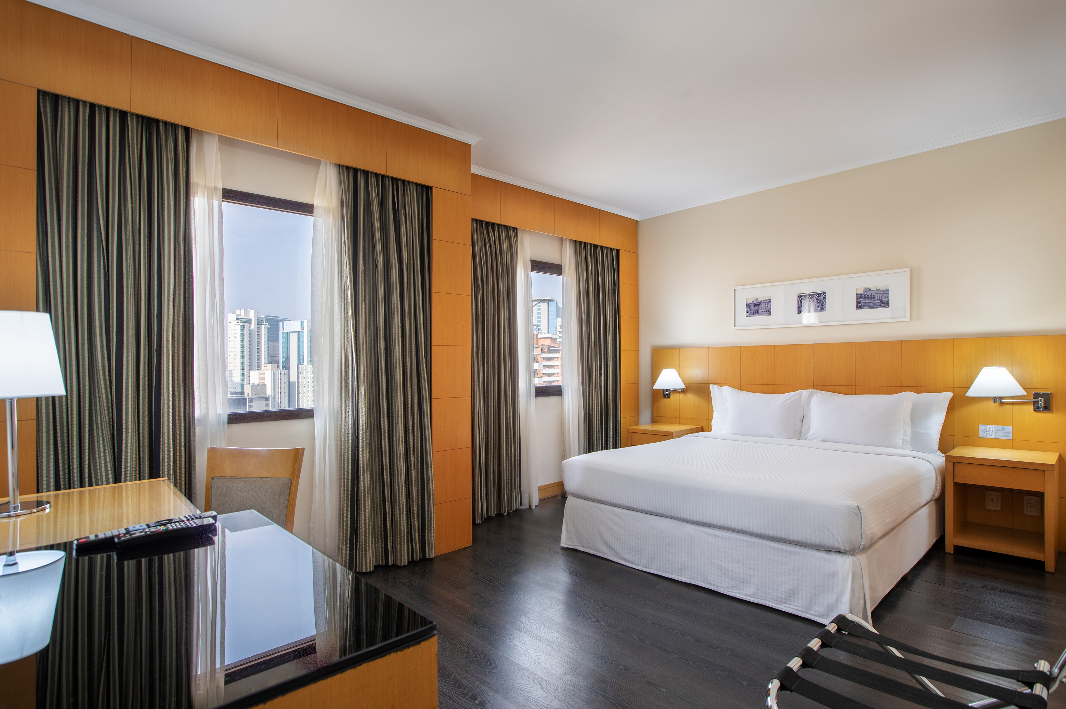 Spacious hotel room with king bed, city view, dark wood floor, and desk.