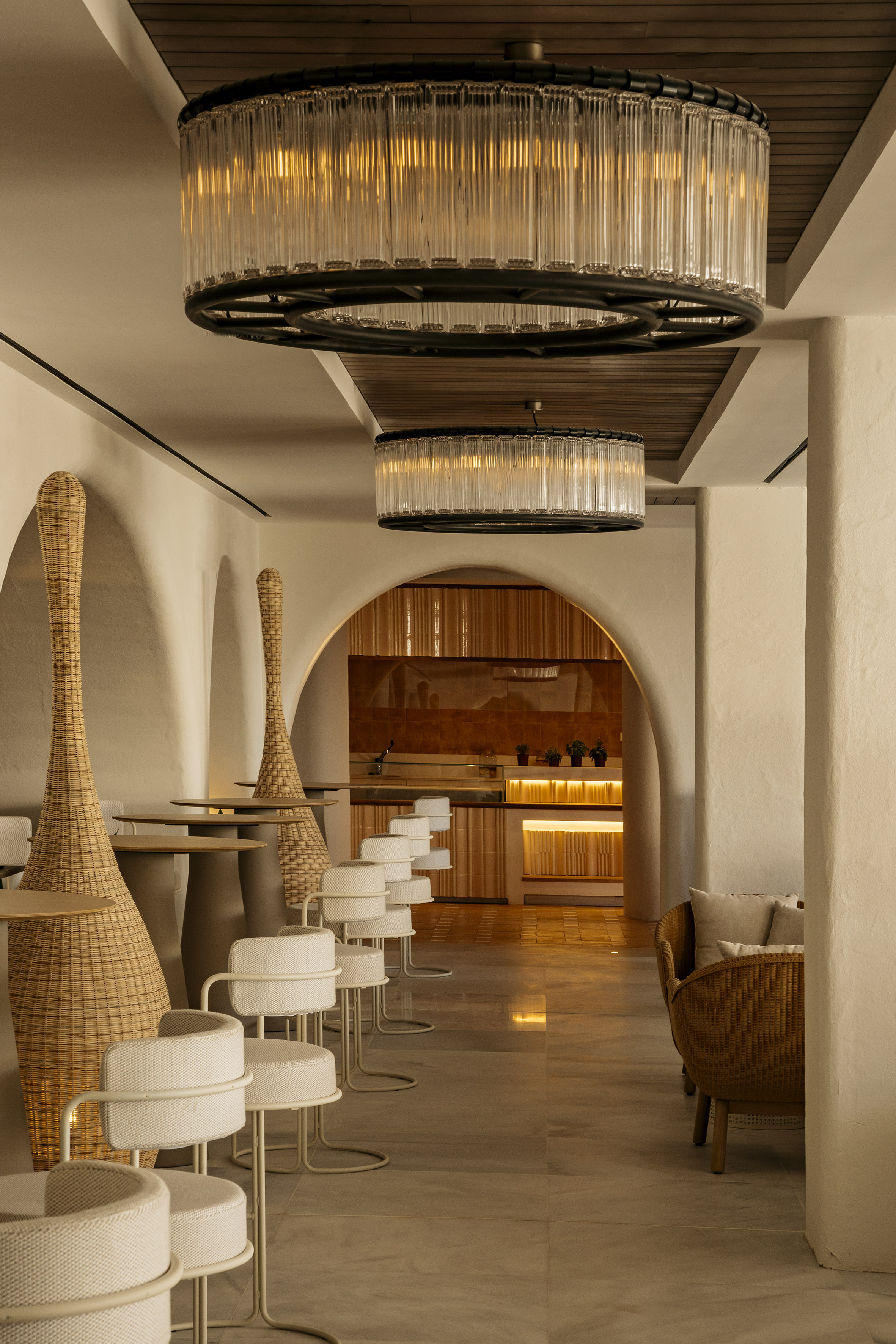 Modern bar lounge with glass chandeliers, rattan seating, and arched walls.