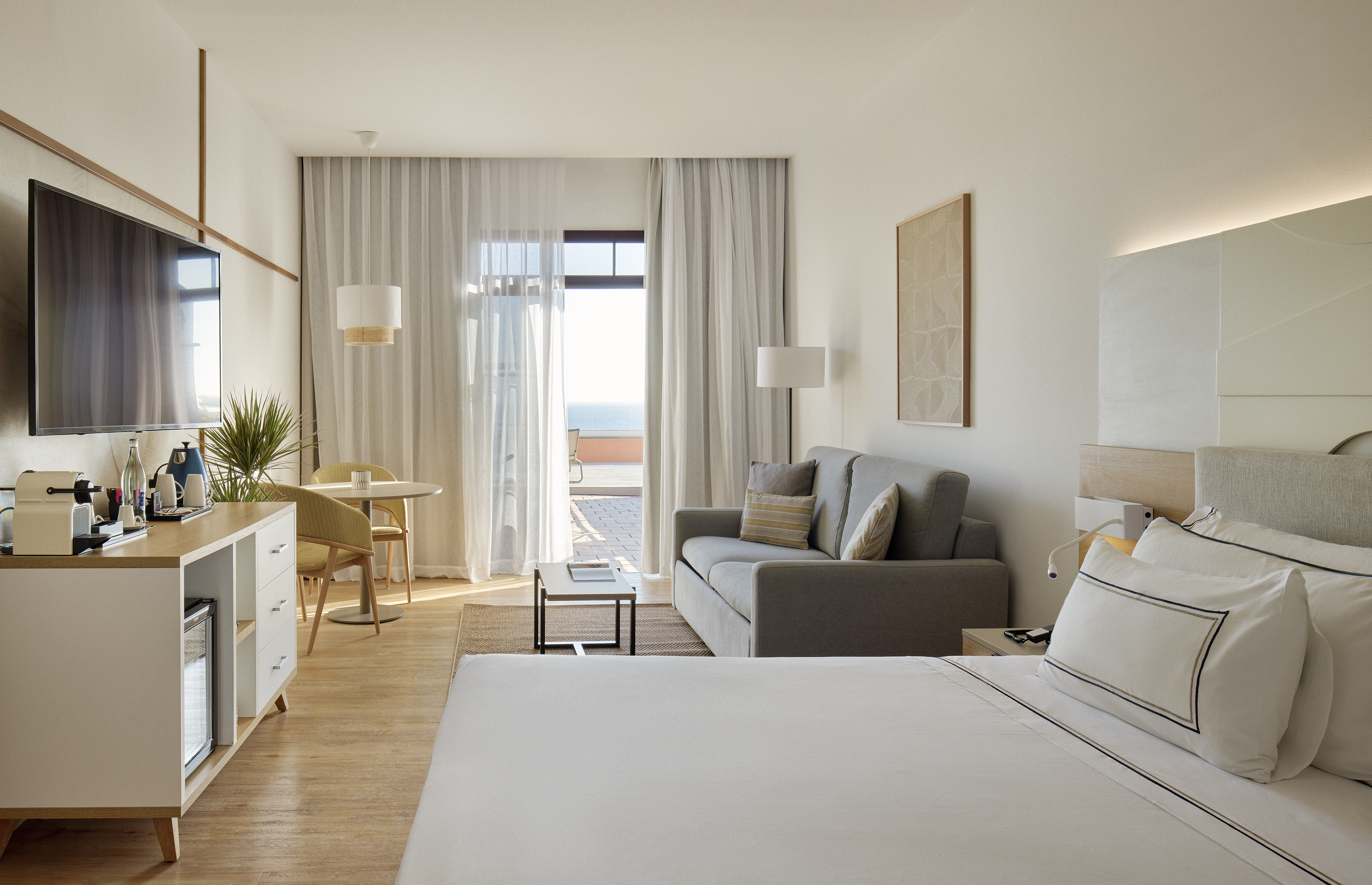 Modern hotel suite with bed, living area, and ocean view balcony.