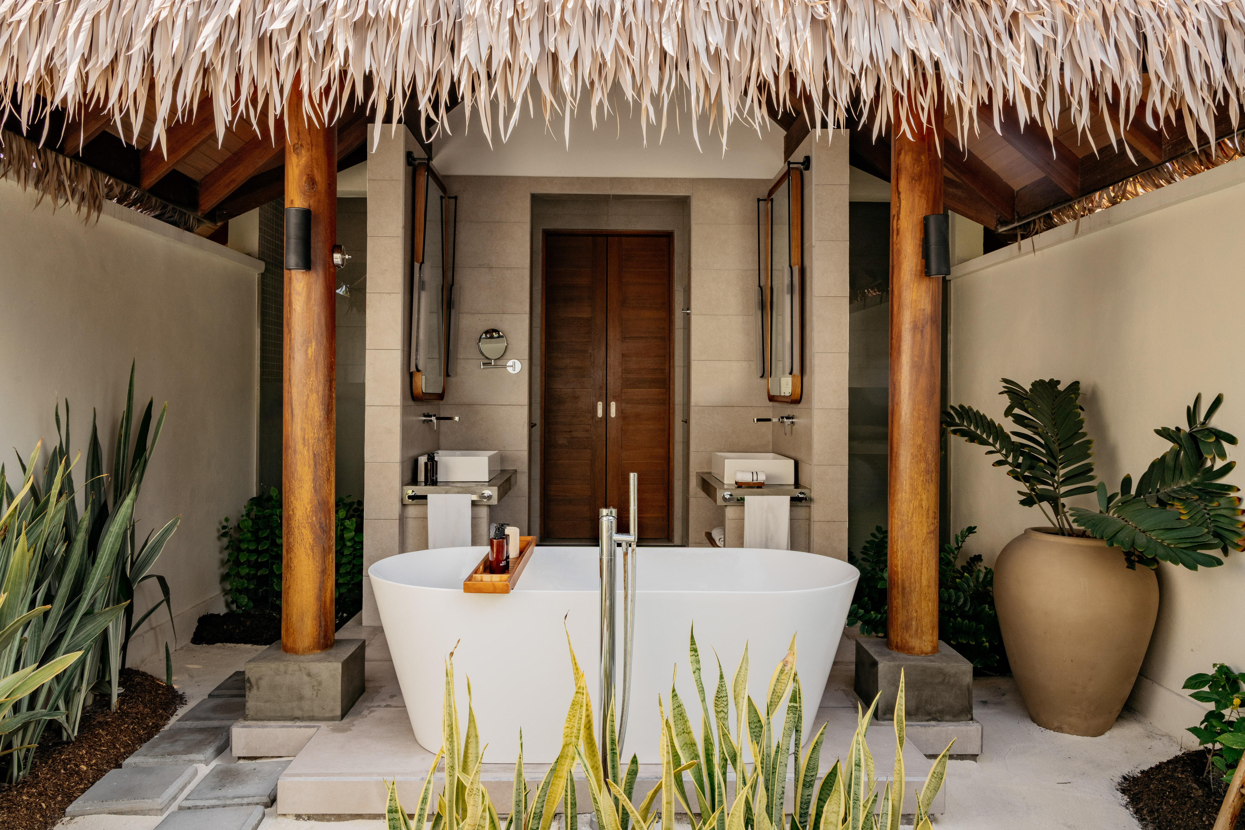 Tropical outdoor bathroom with freestanding tub and thatched roof.