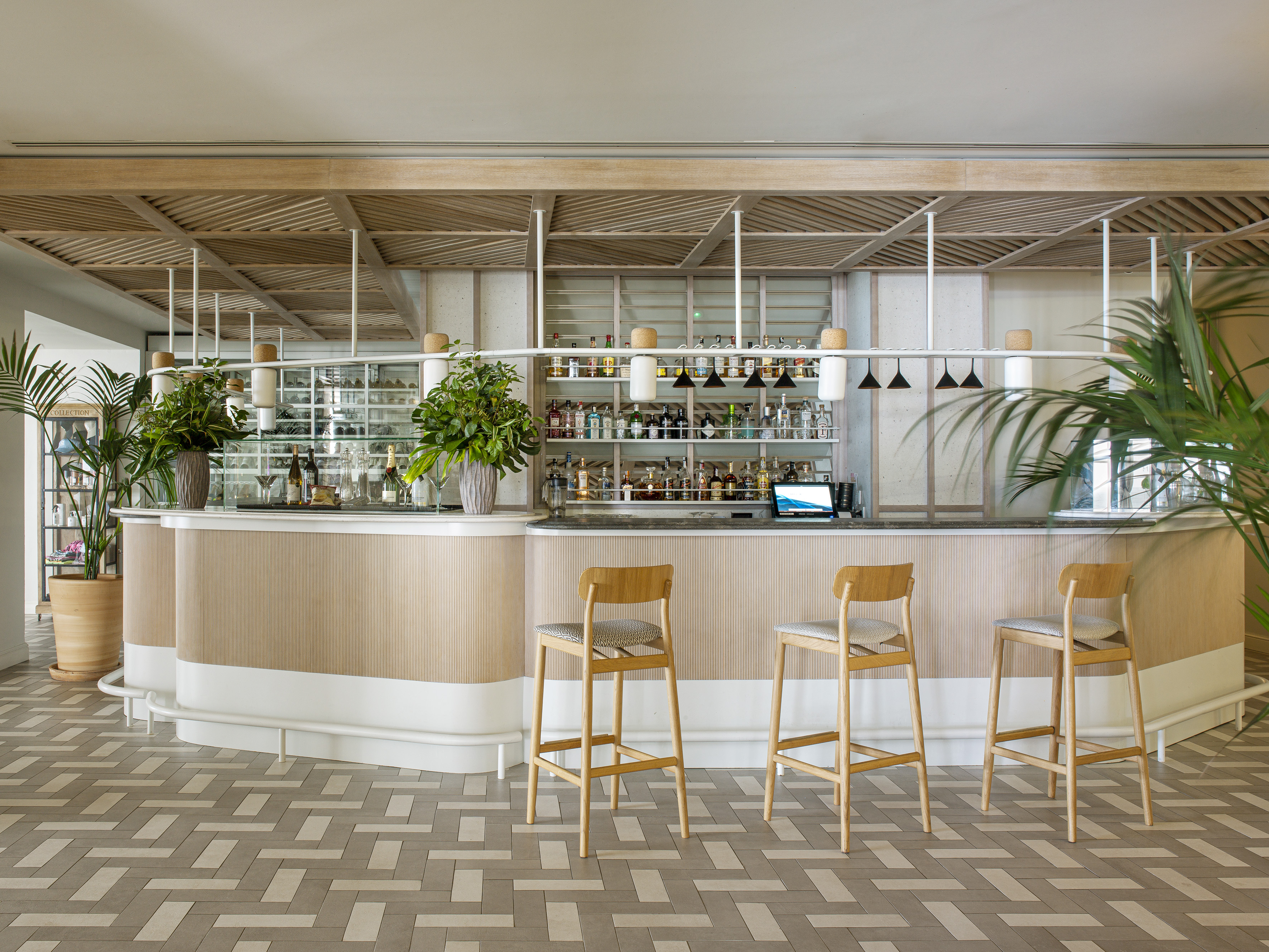 Contemporary bar with light wood counter, bar stools, liquor display, and patterned floor.