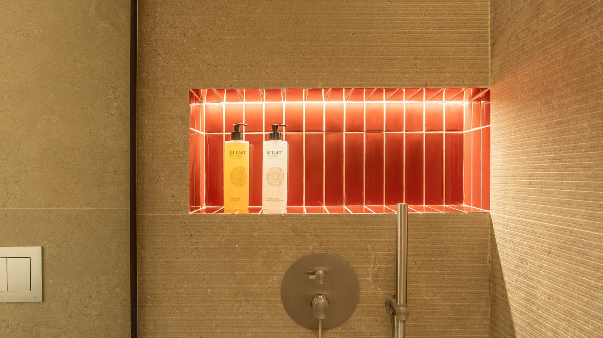 Modern shower with backlit red tile niche, argan products, and textured beige walls.