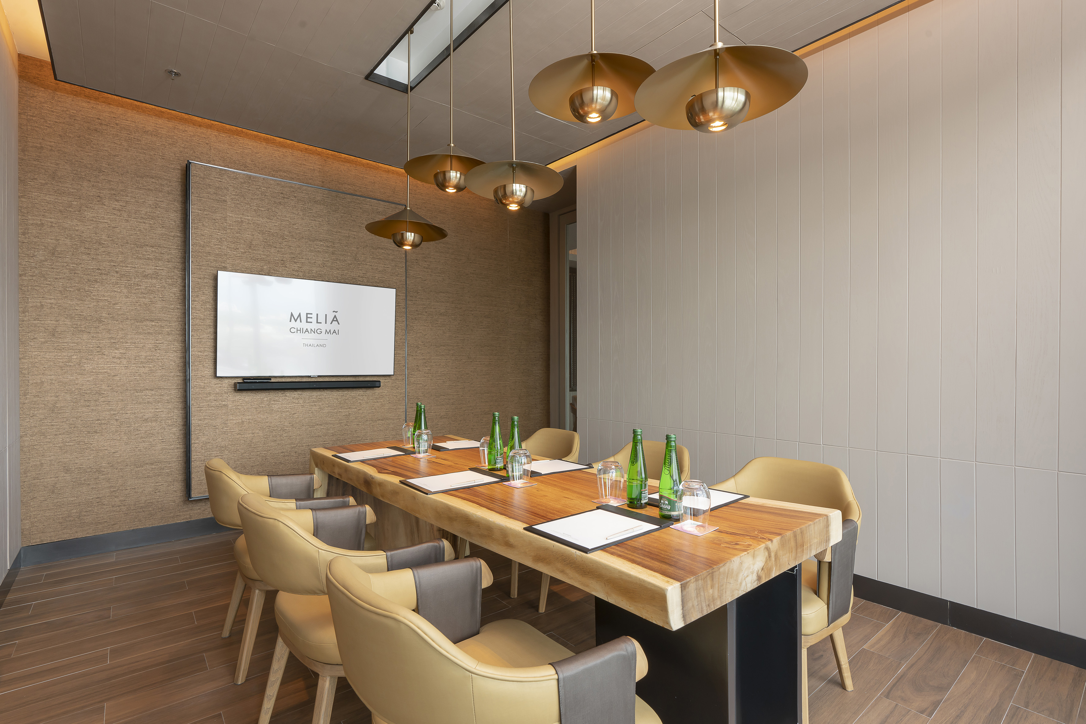 Meliá Chiang Mai meeting room with modern wood table, tan chairs, and screen.
