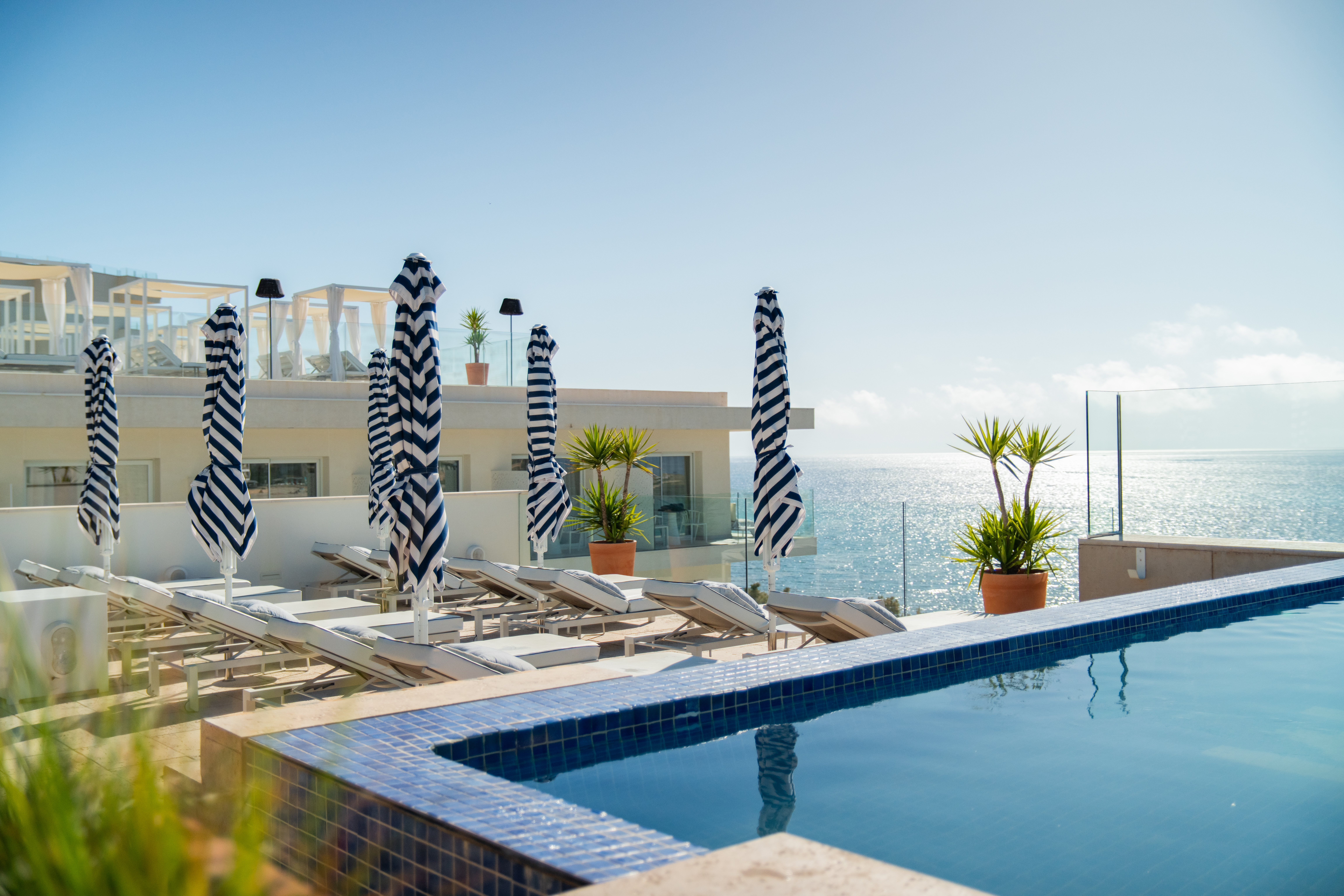 Piscina infinita, tumbonas y sombrillas a rayas con vistas al mar en resort.
