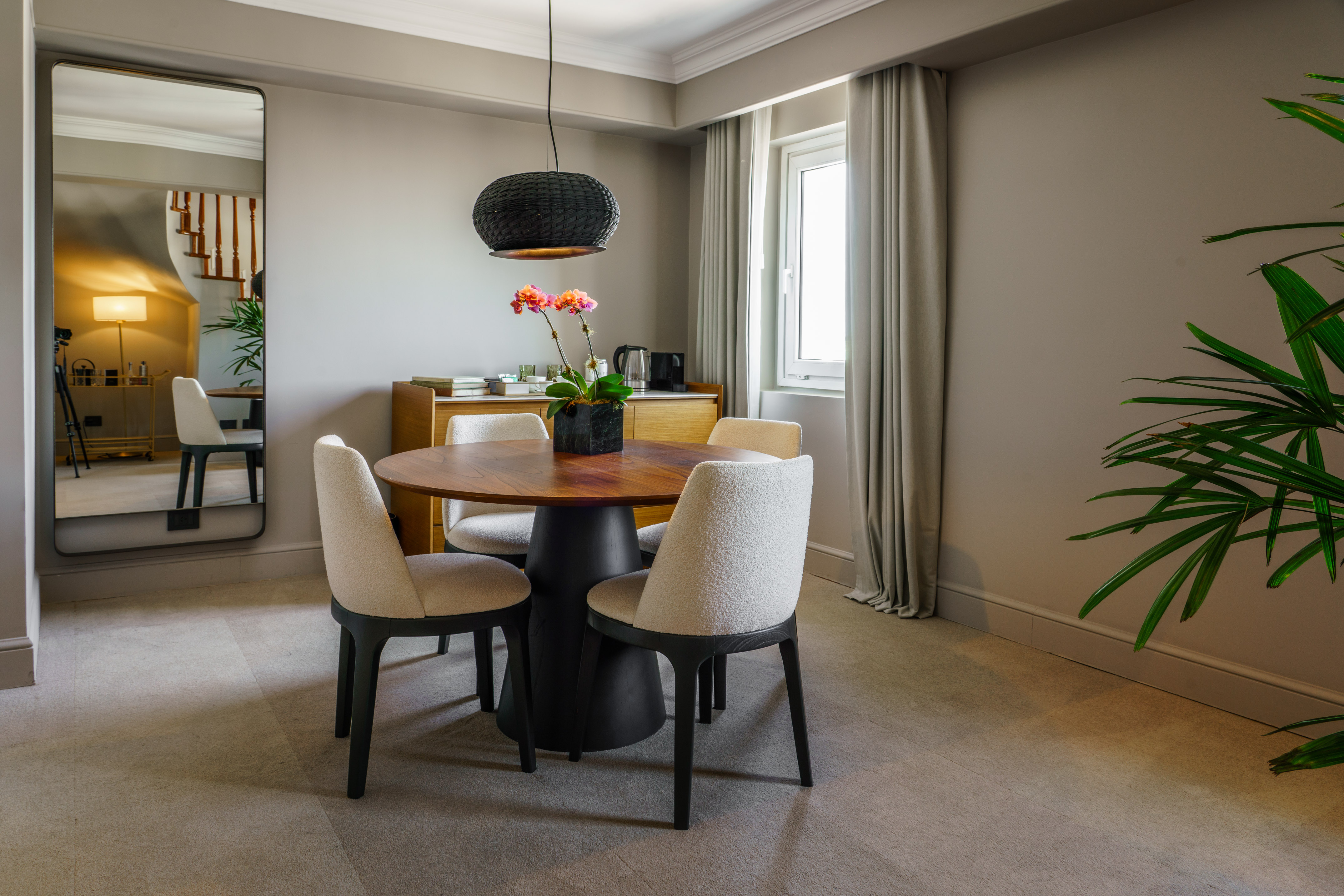 Elegant dining area with round wooden table, modern chairs, black pendant light.