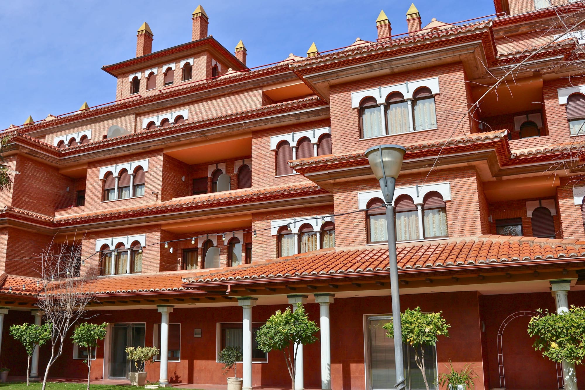 Spanish-style red brick building, terracotta roof, arched windows, blue sky.