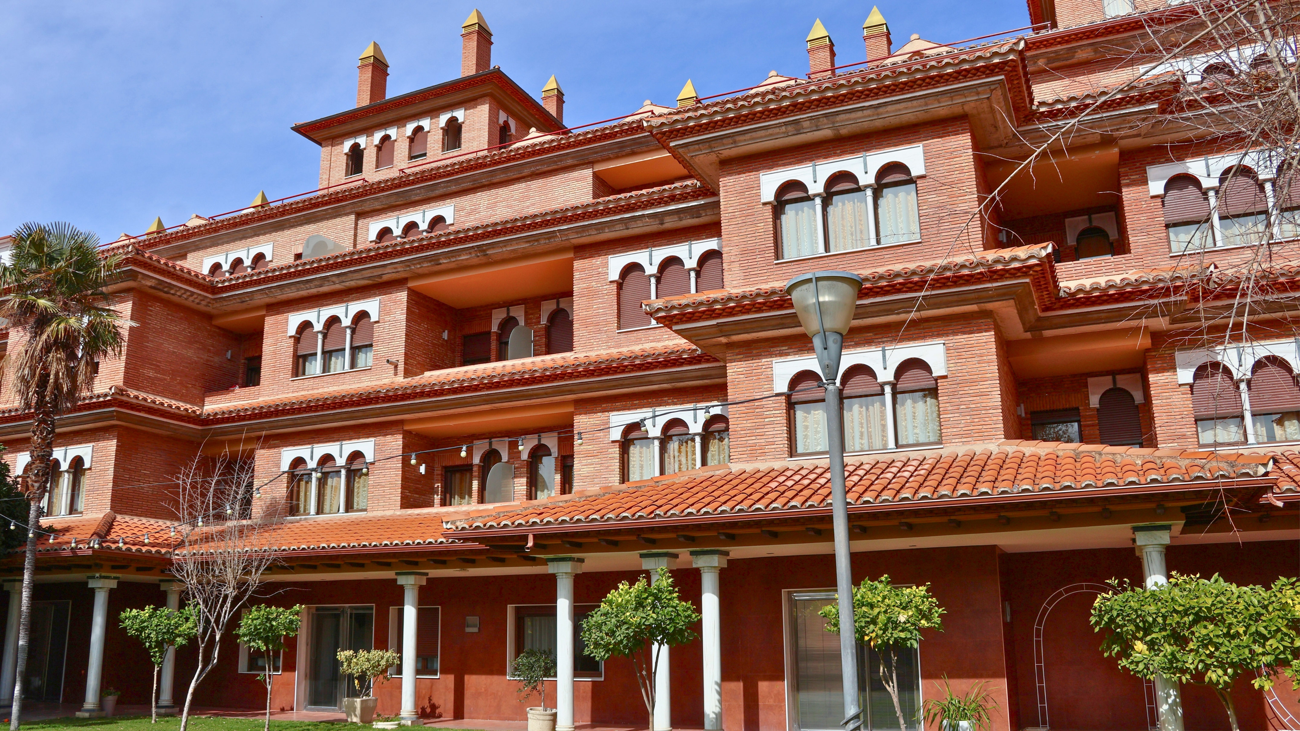 Spanish-style red brick building, terracotta roof, arched windows, blue sky.