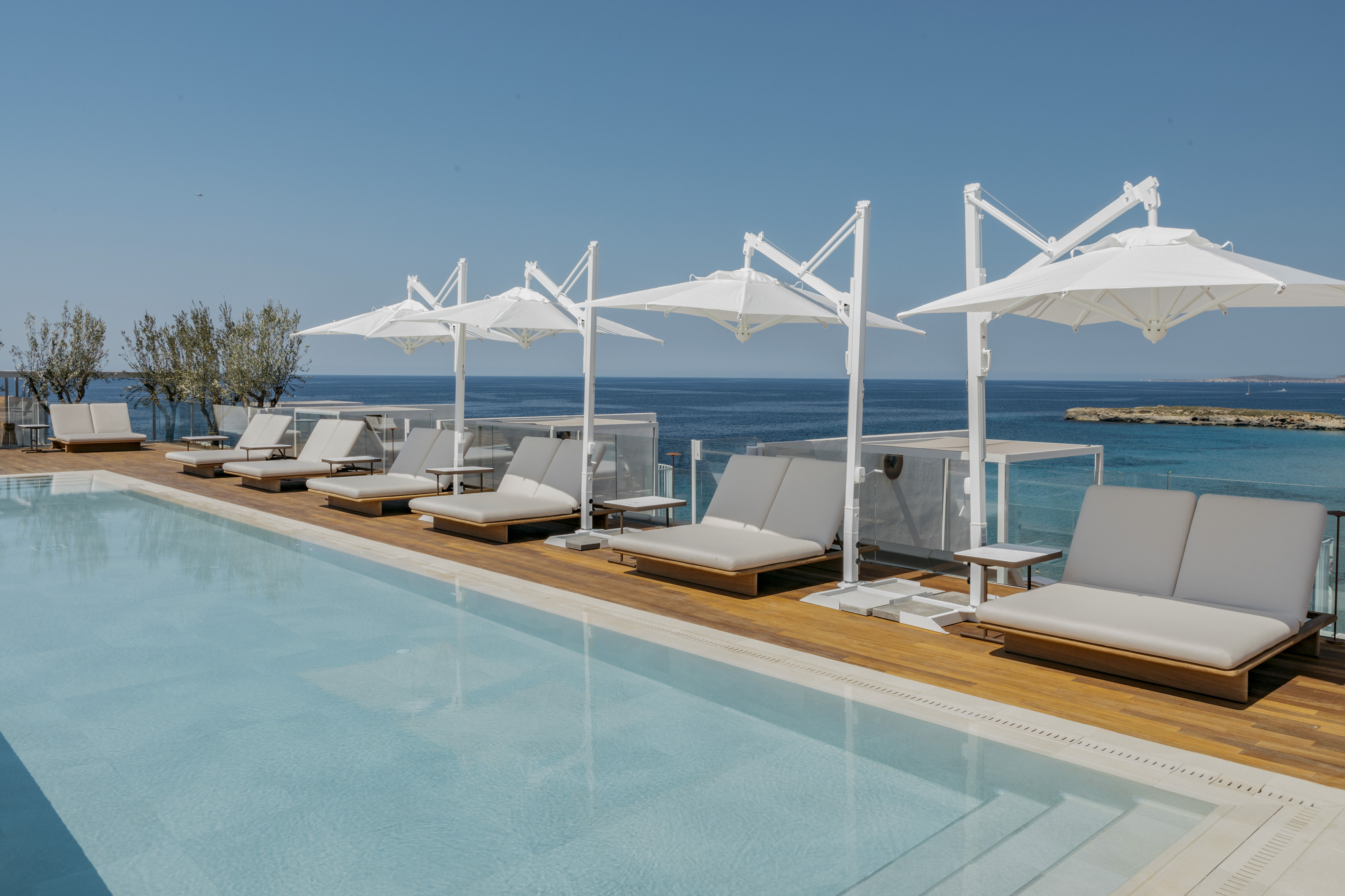 Oceanfront hotel pool with sun loungers and white parasols on wooden deck.