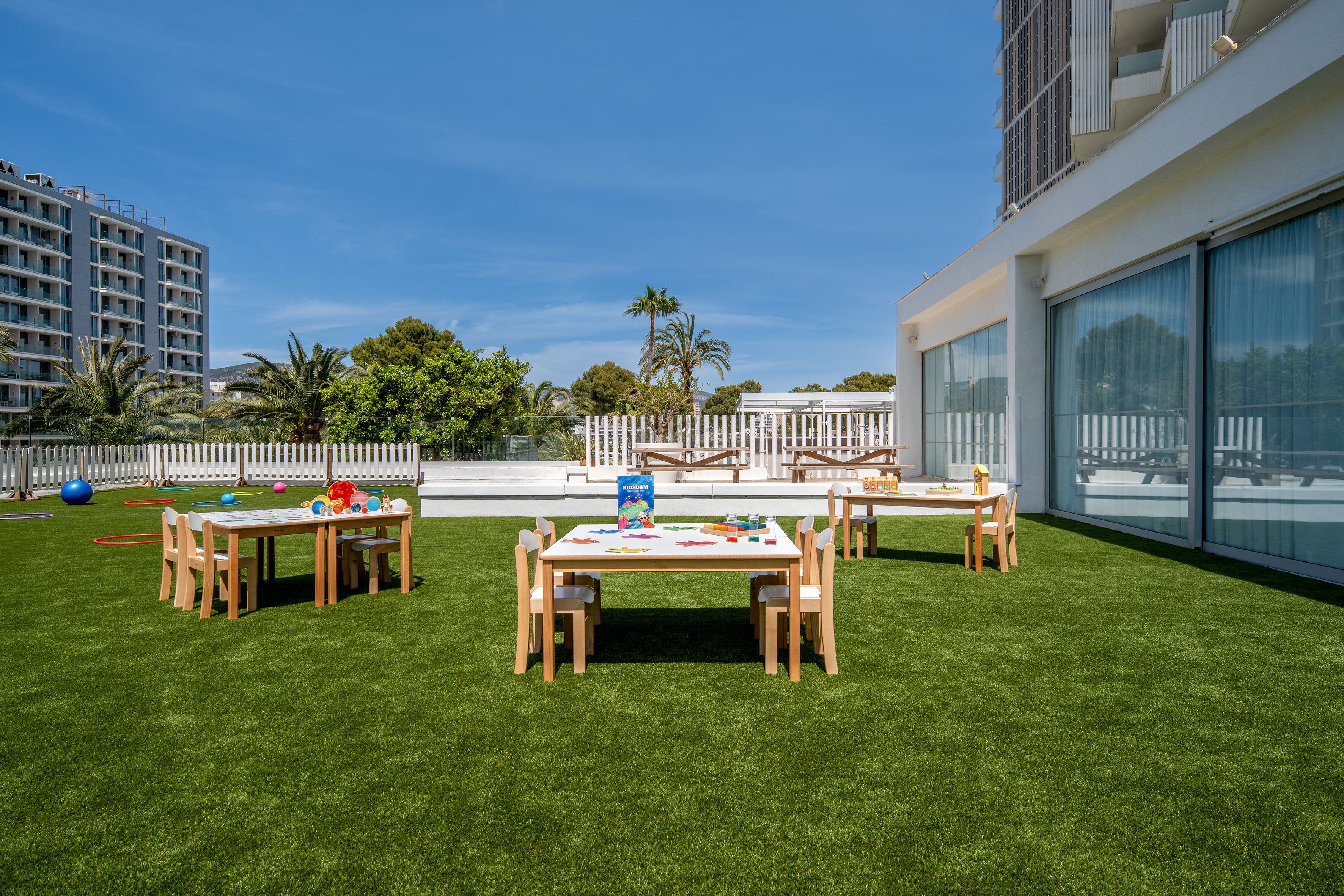 Outdoor kids' club with activity tables, chairs on artificial grass.