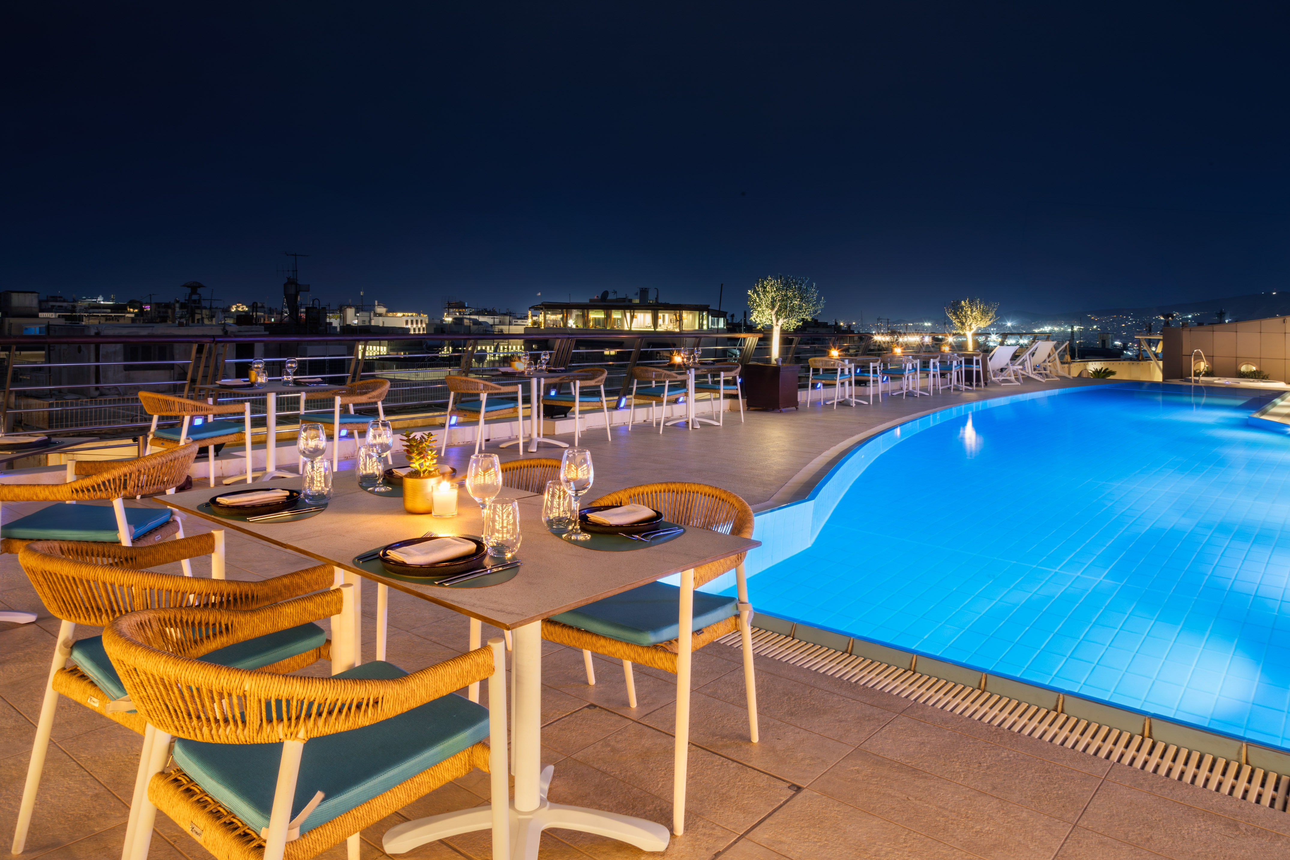 Rooftop dining, candlelit tables, sparkling blue pool, and night city view.
