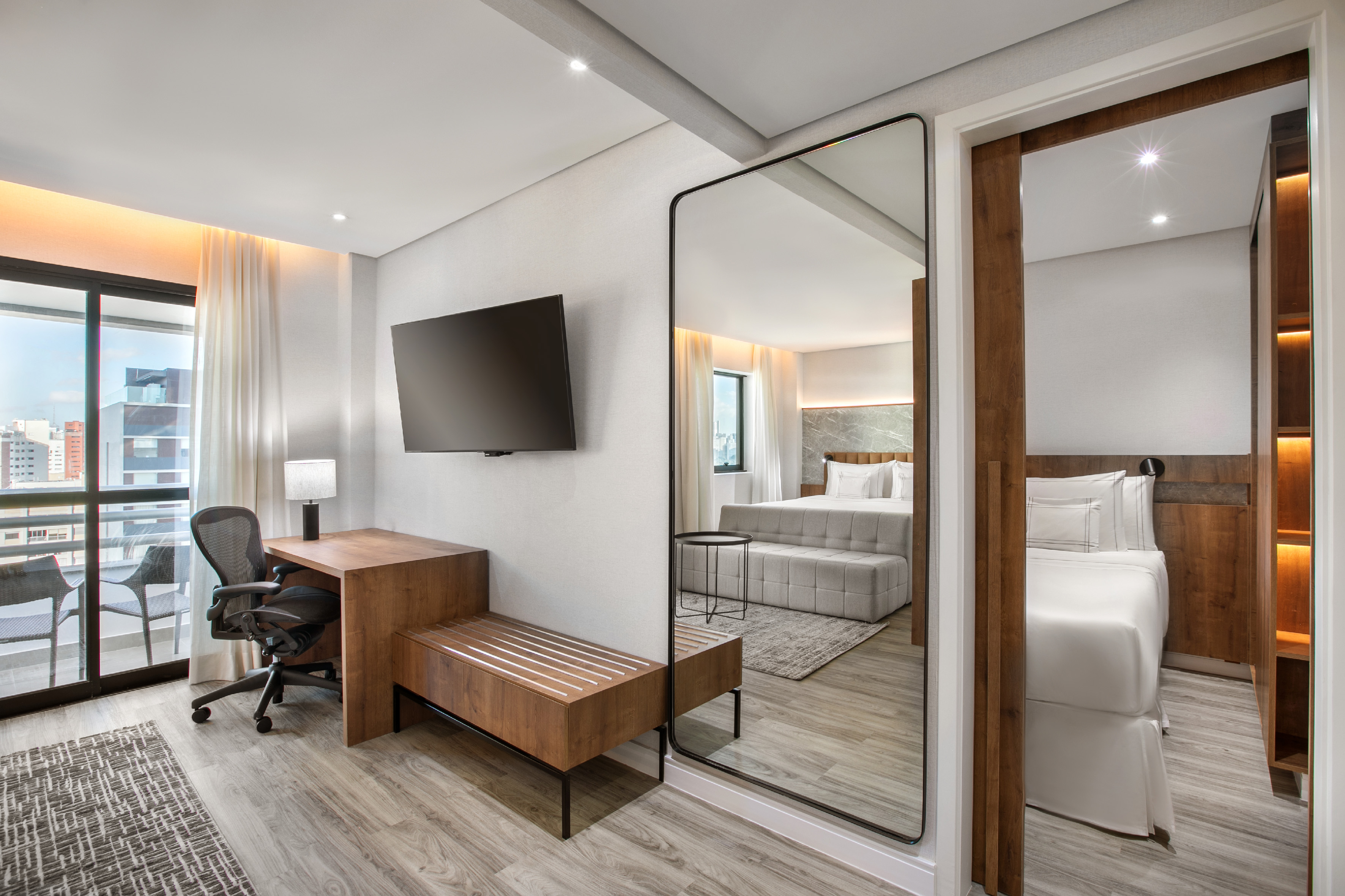 Modern hotel room with desk, TV, mirror, and balcony view.