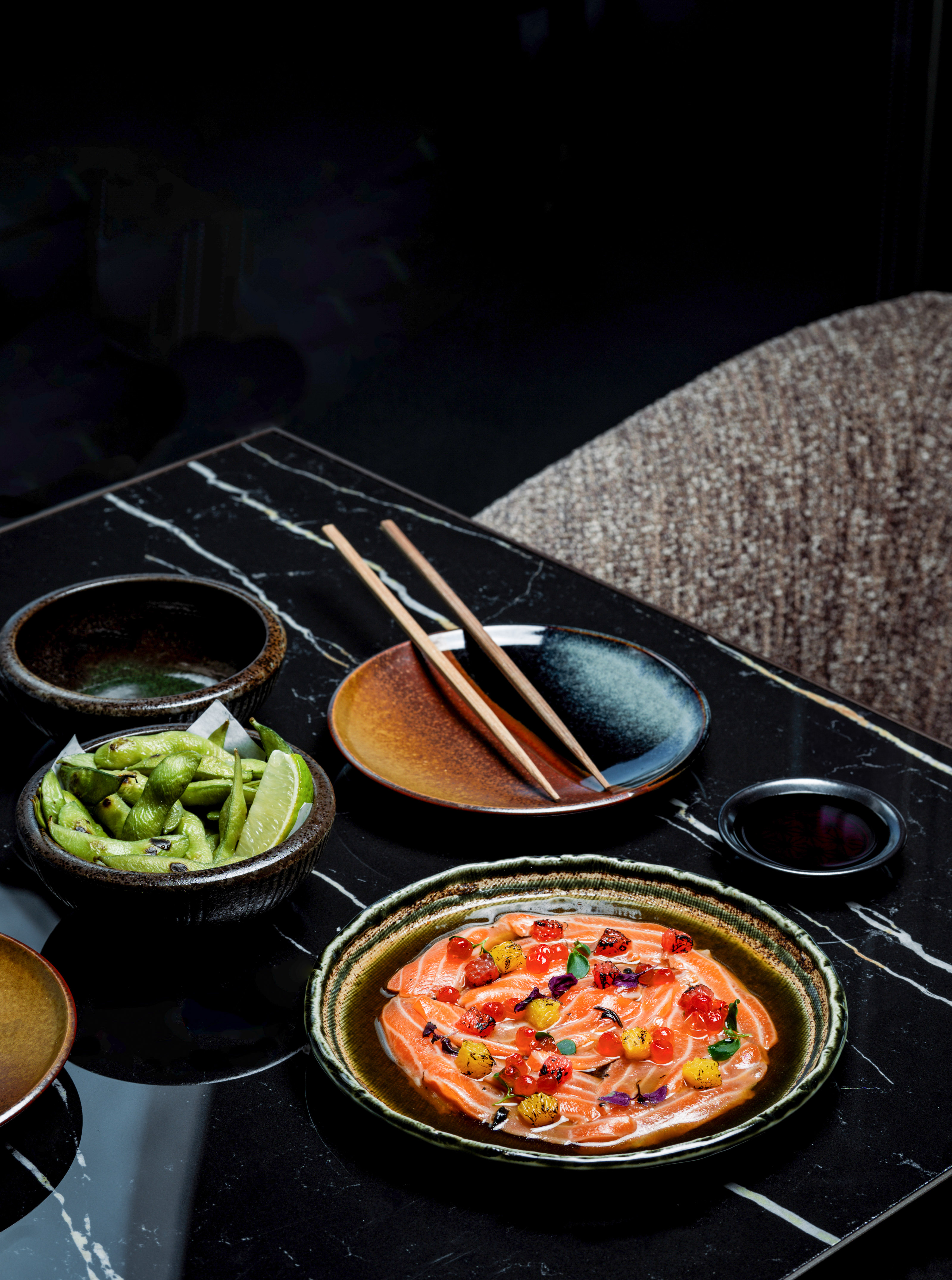 Salmon carpaccio, edamame, and chopsticks on a dark marble table.