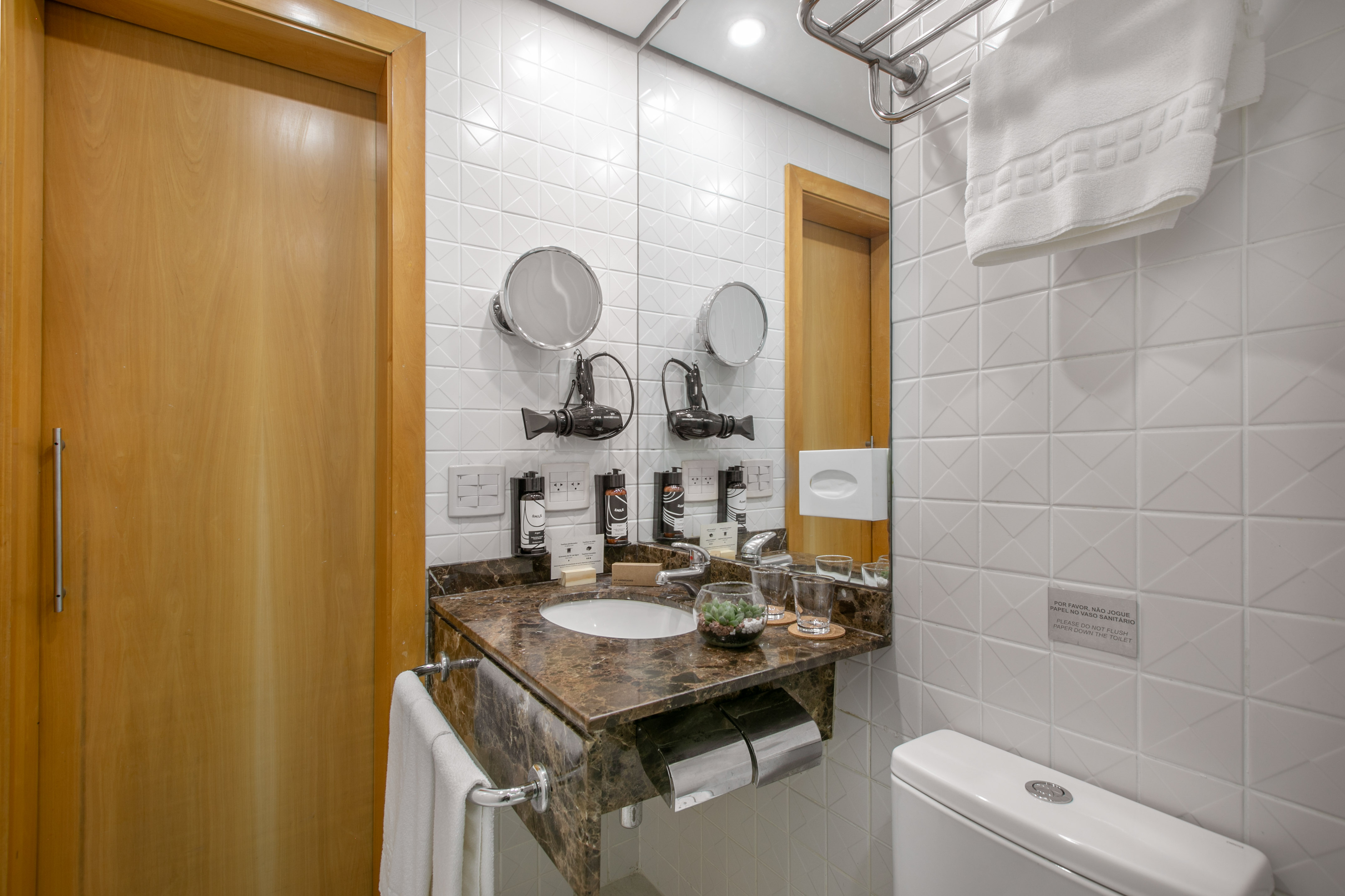 Modern hotel bathroom with marble vanity, sink, mirror, toiletries, and toilet.