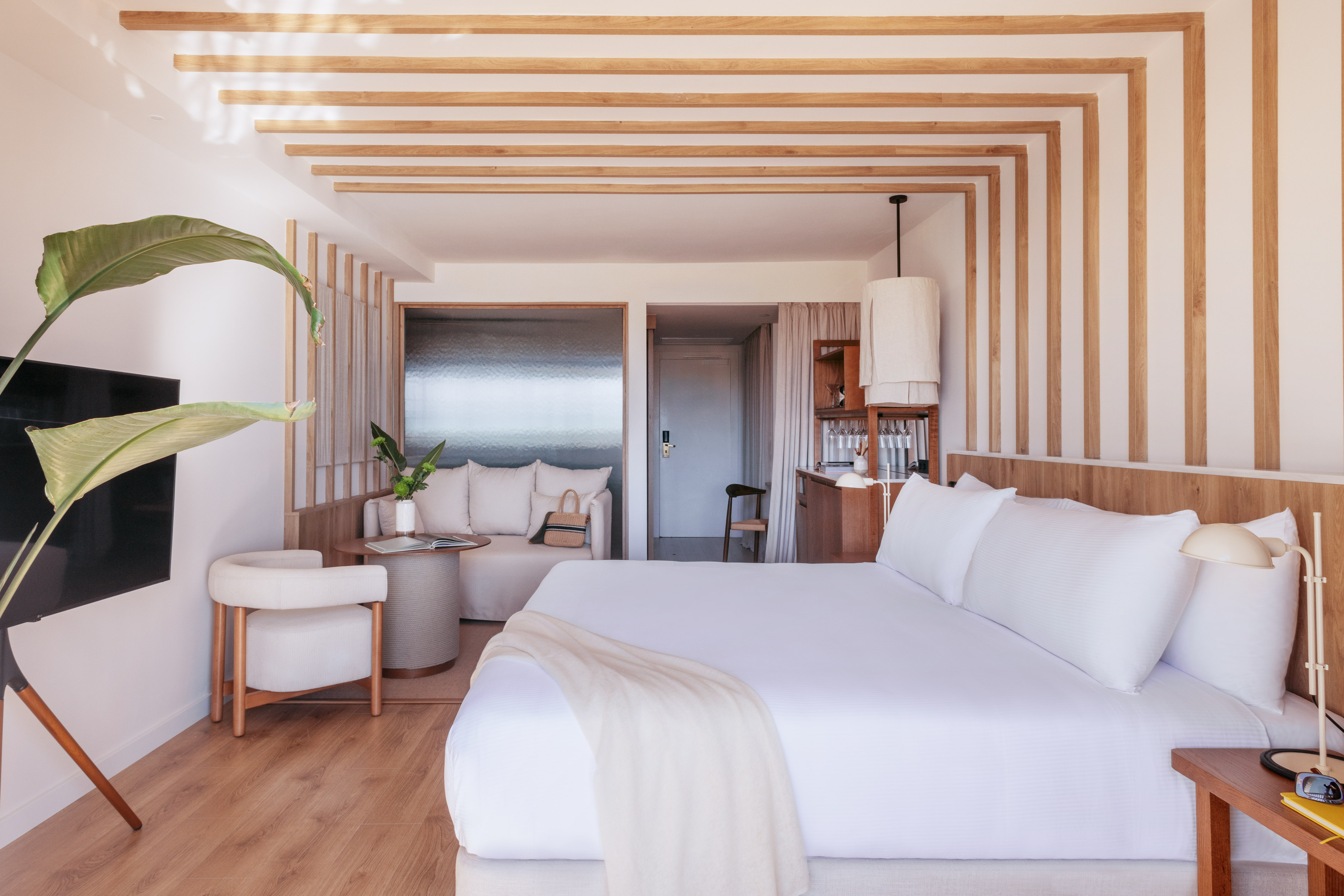 Modern hotel suite with white bed, lounge area, and natural wood design. - Always ME Connecting - ME Marbella, Marbella
