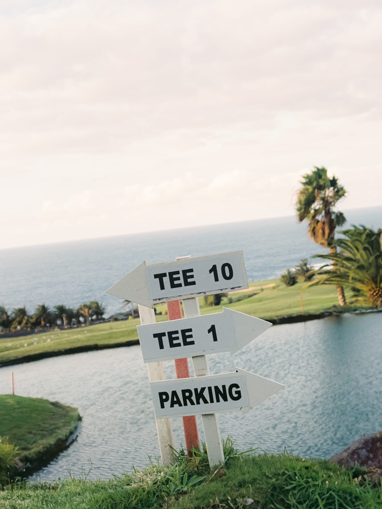 Golf course sign: Tee 10, Tee 1, Parking, with water and palm trees.