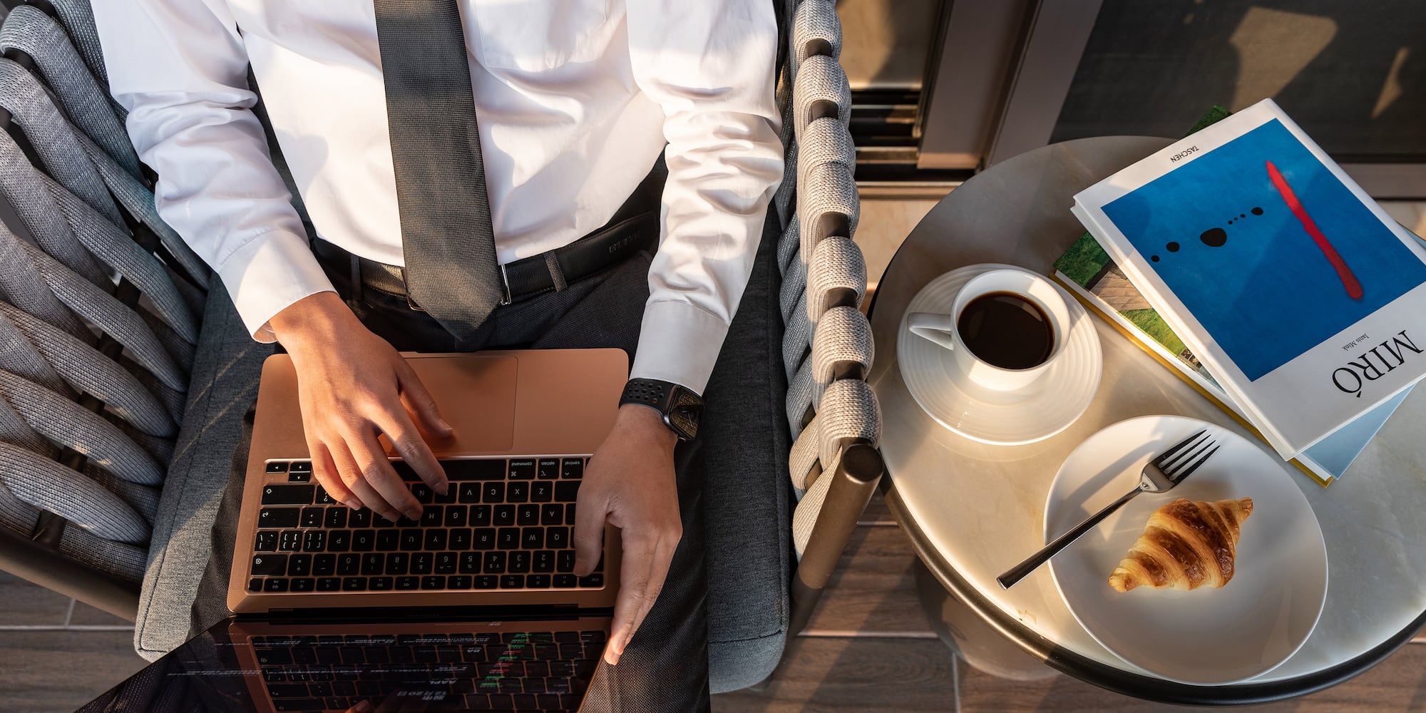 a man sitting in a chair with a laptop and a croissant