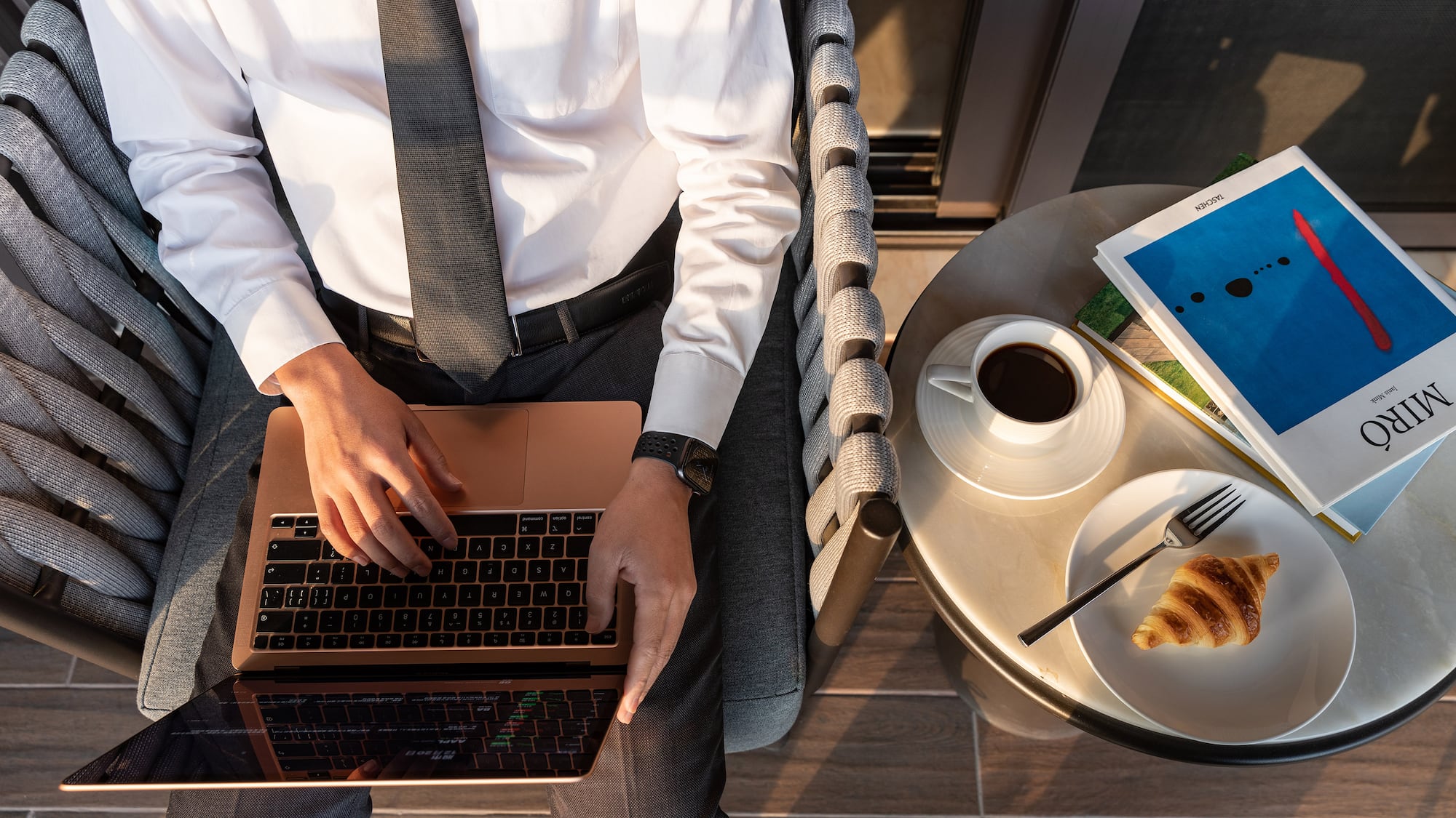 a man sitting in a chair with a laptop and a croissant