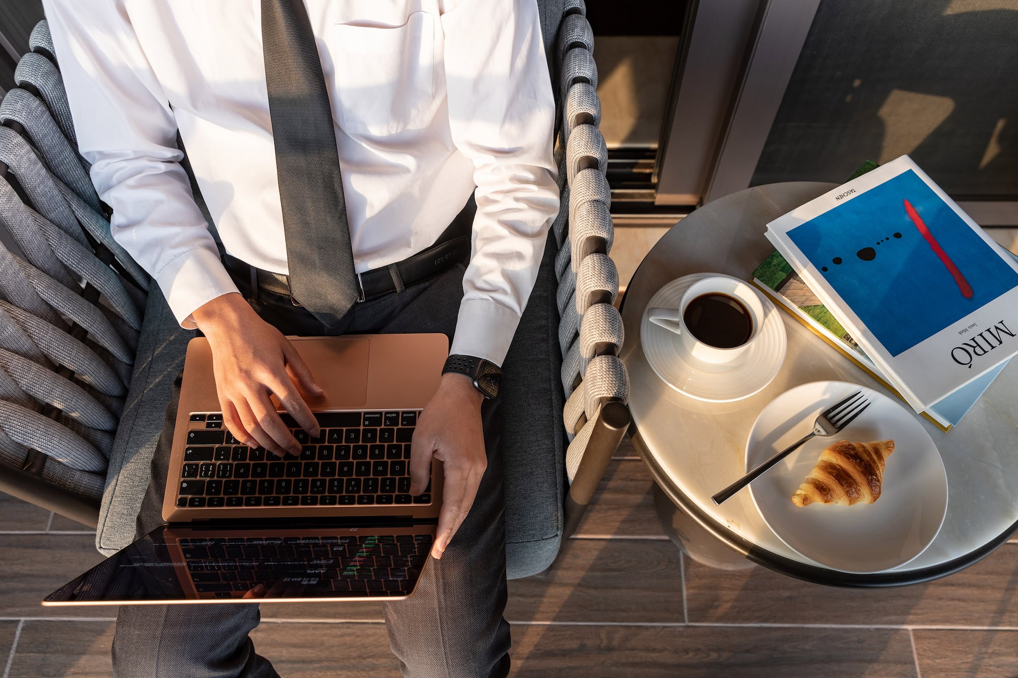 a man sitting in a chair with a laptop and a croissant