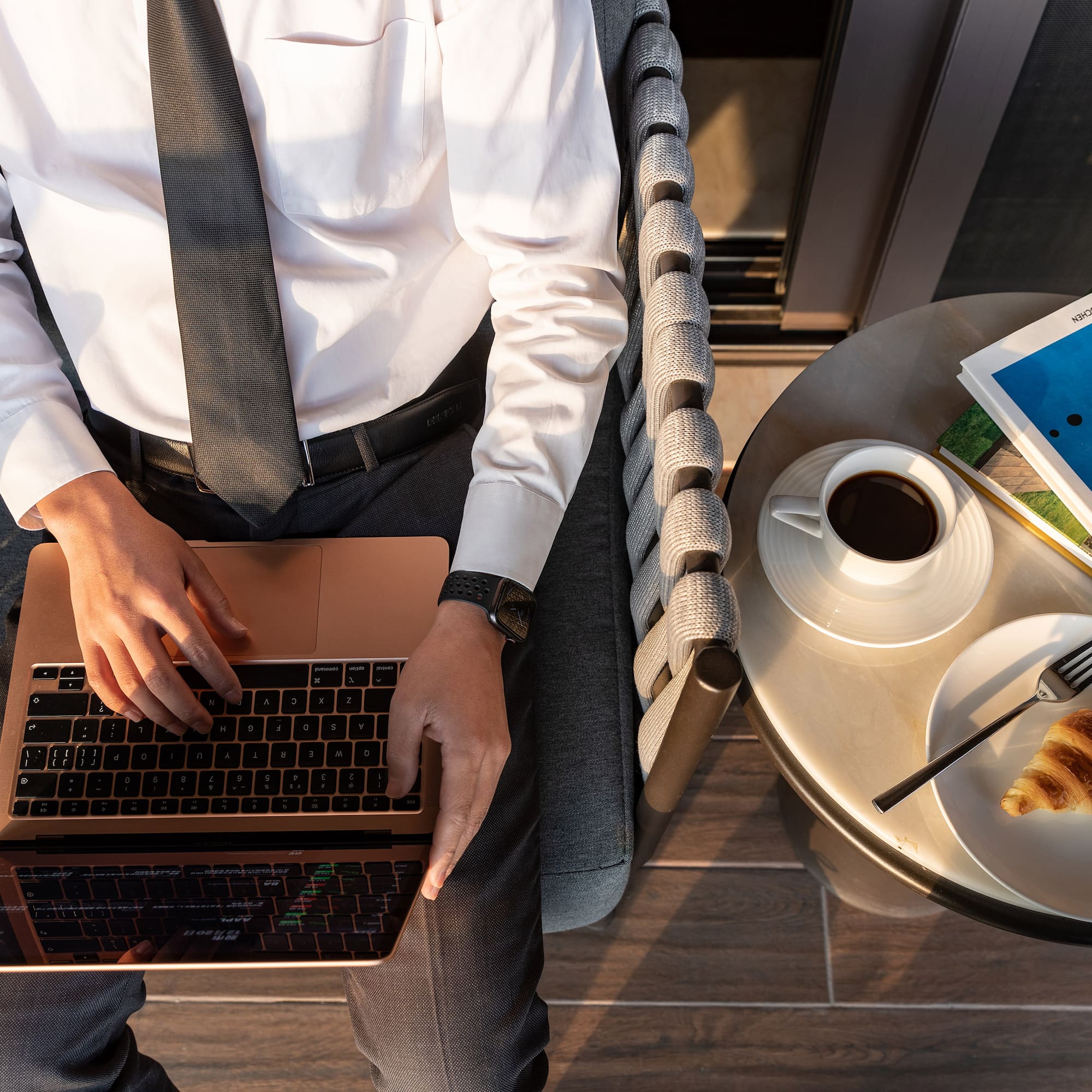 a man sitting in a chair with a laptop and a croissant
