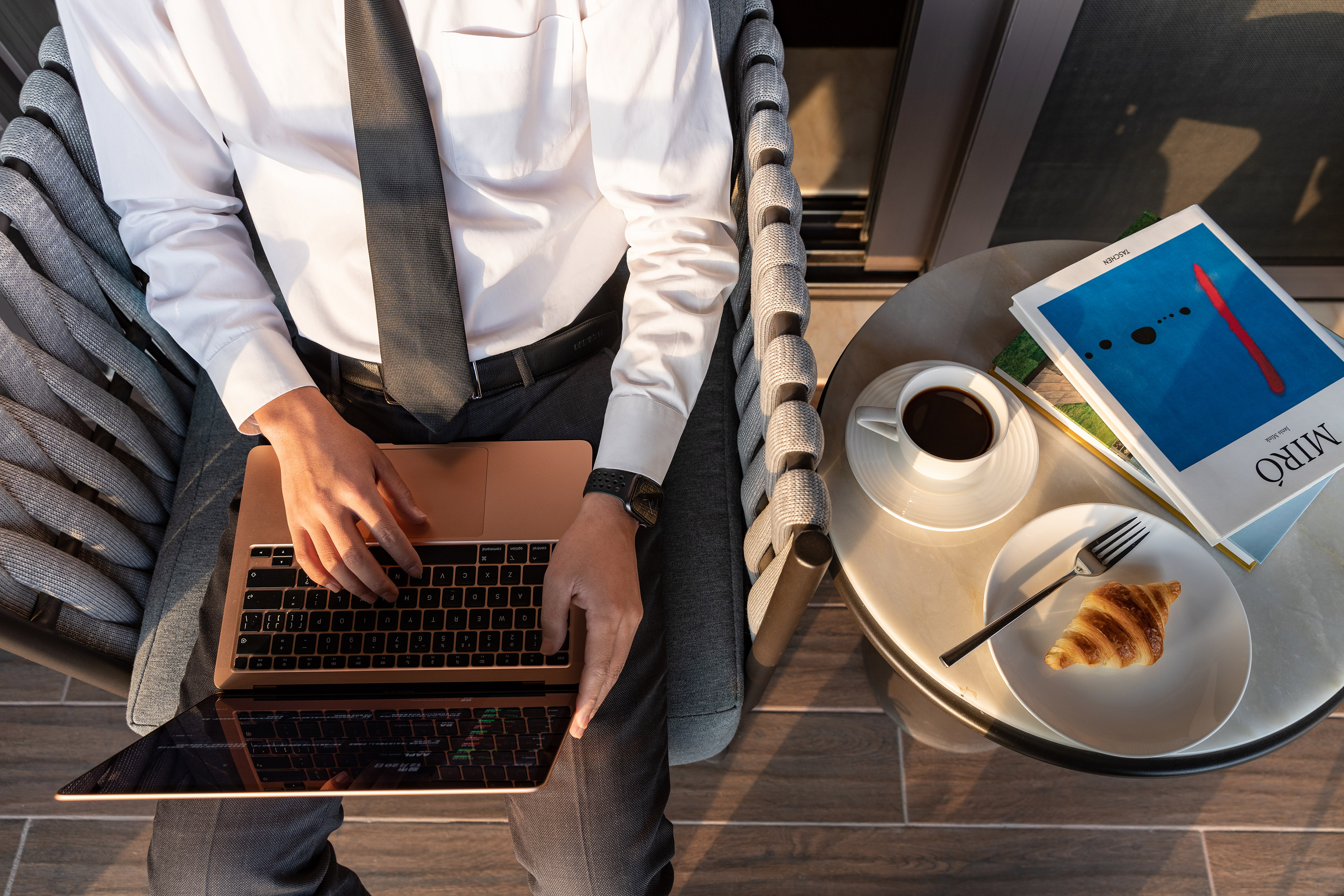 a man sitting in a chair with a laptop and a croissant