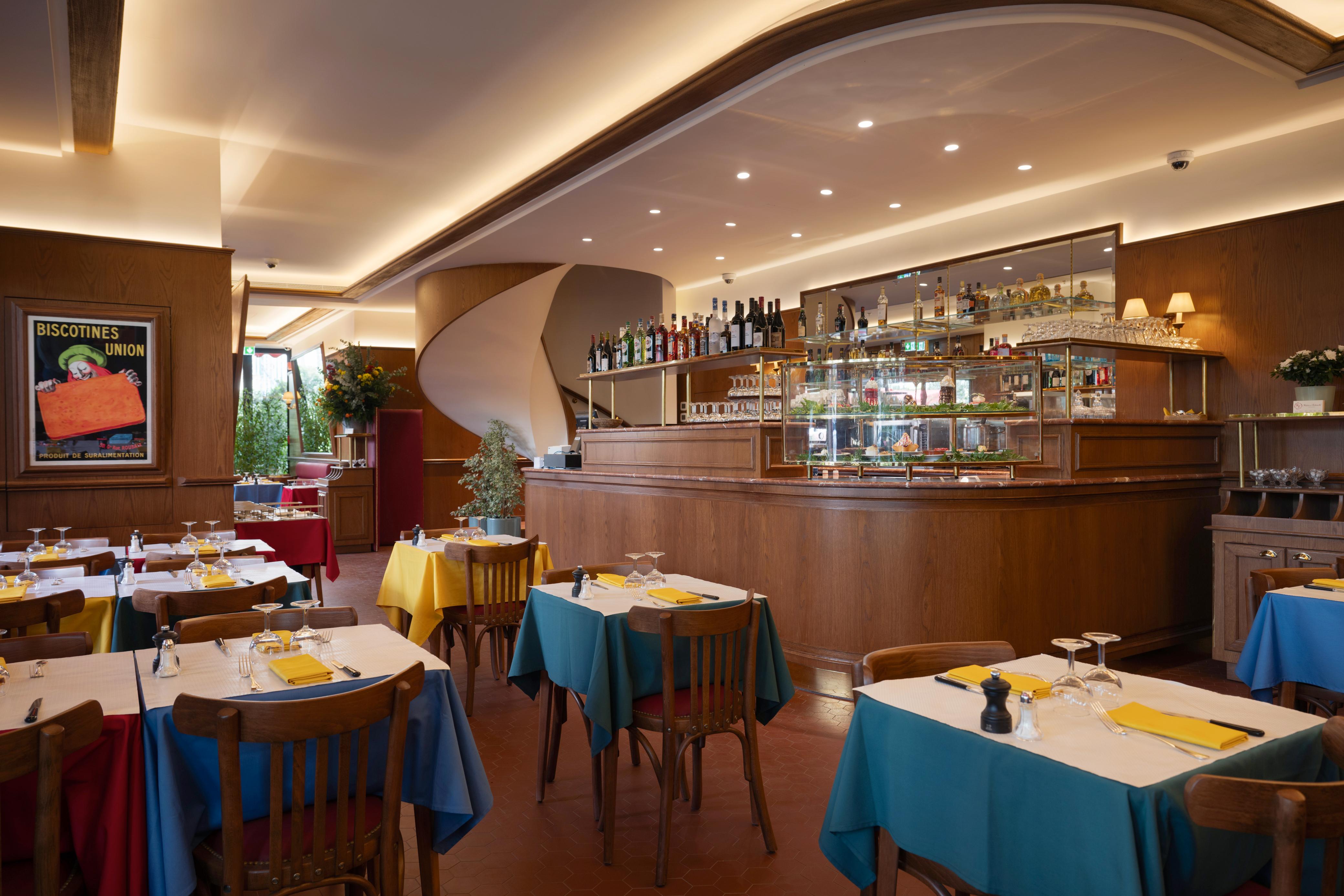 Restaurant dining room with colorful tables, wooden bar, and spiral staircase.