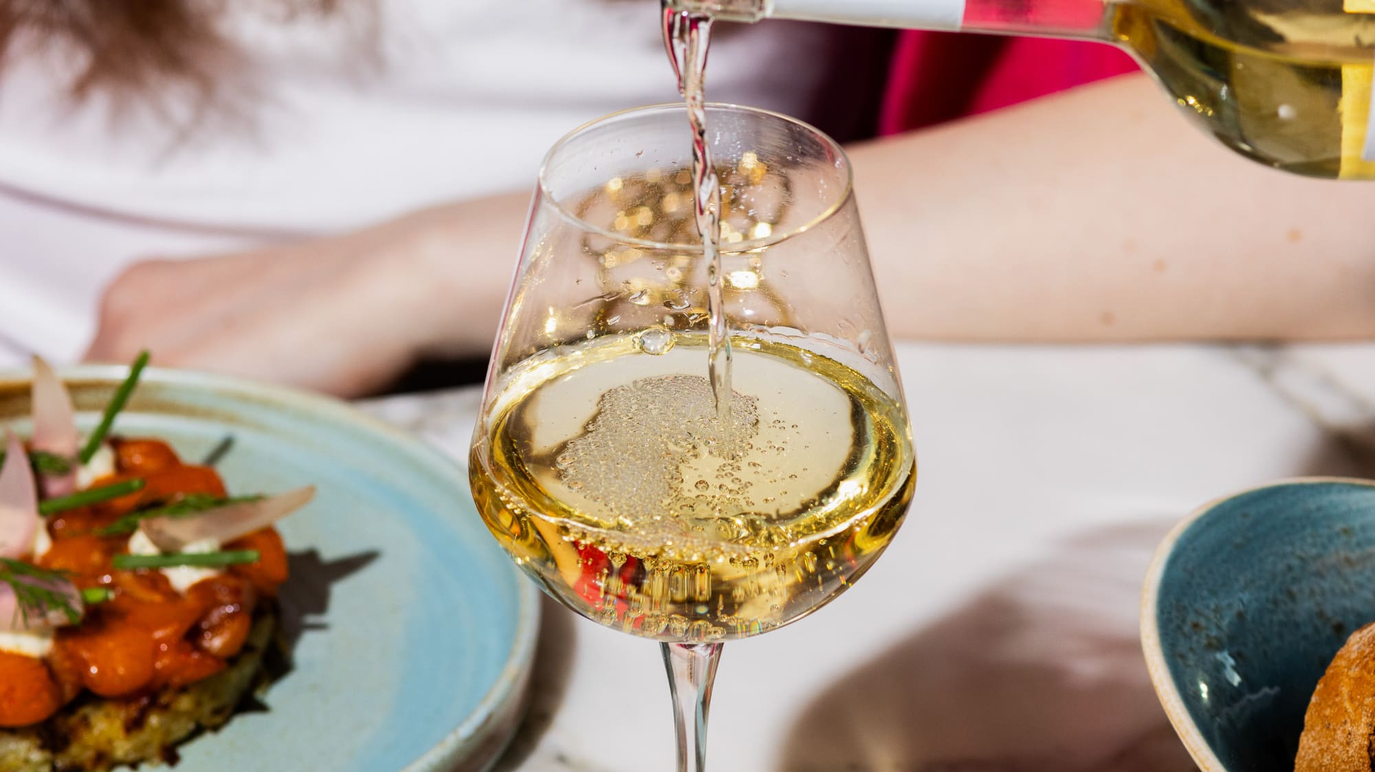 Pouring Savini sparkling wine into a glass. Appetizers on a marble table.