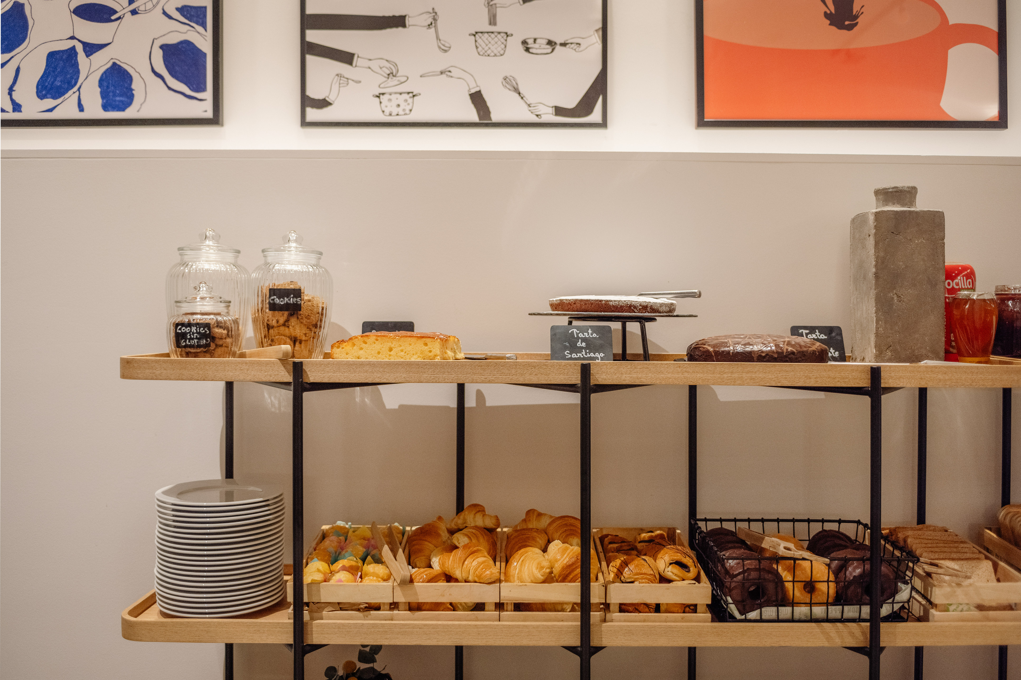 Breakfast buffet with various cakes, cookies, croissants, and donuts on a wooden shelf.