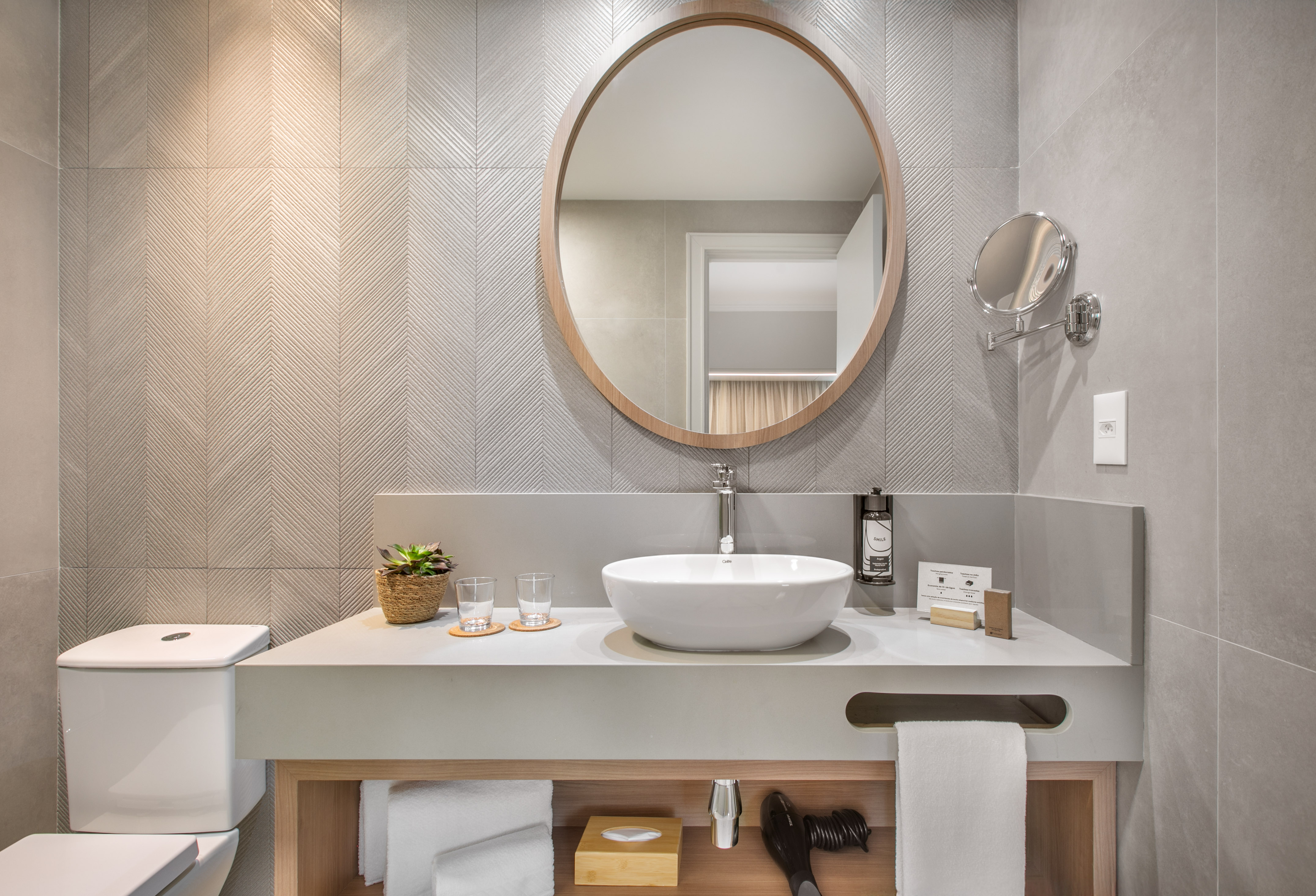 Contemporary bathroom vanity with round wood mirror, vessel sink, grey tiles.