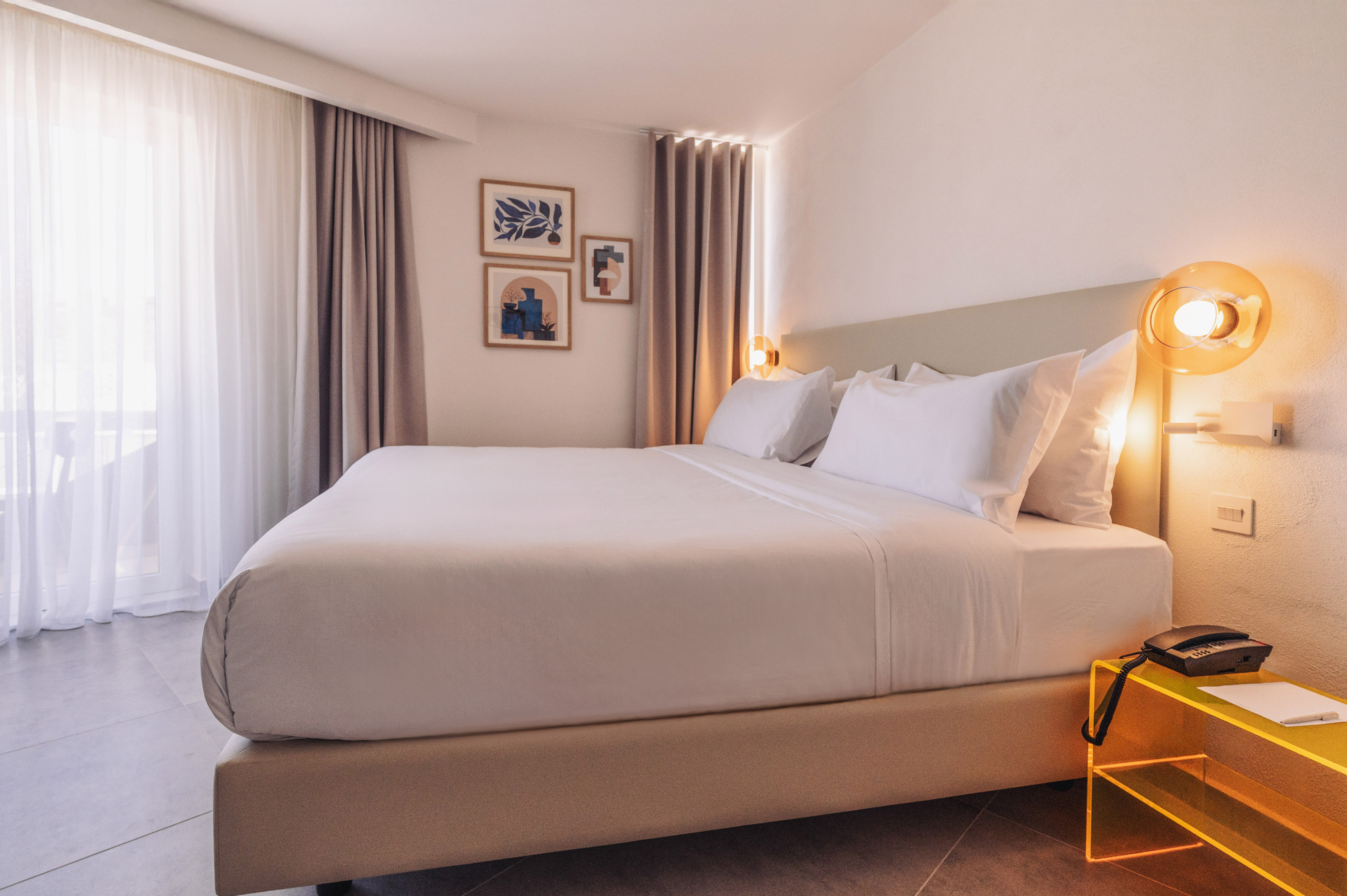 Modern hotel bedroom with white bed, contemporary decor, and abstract art.