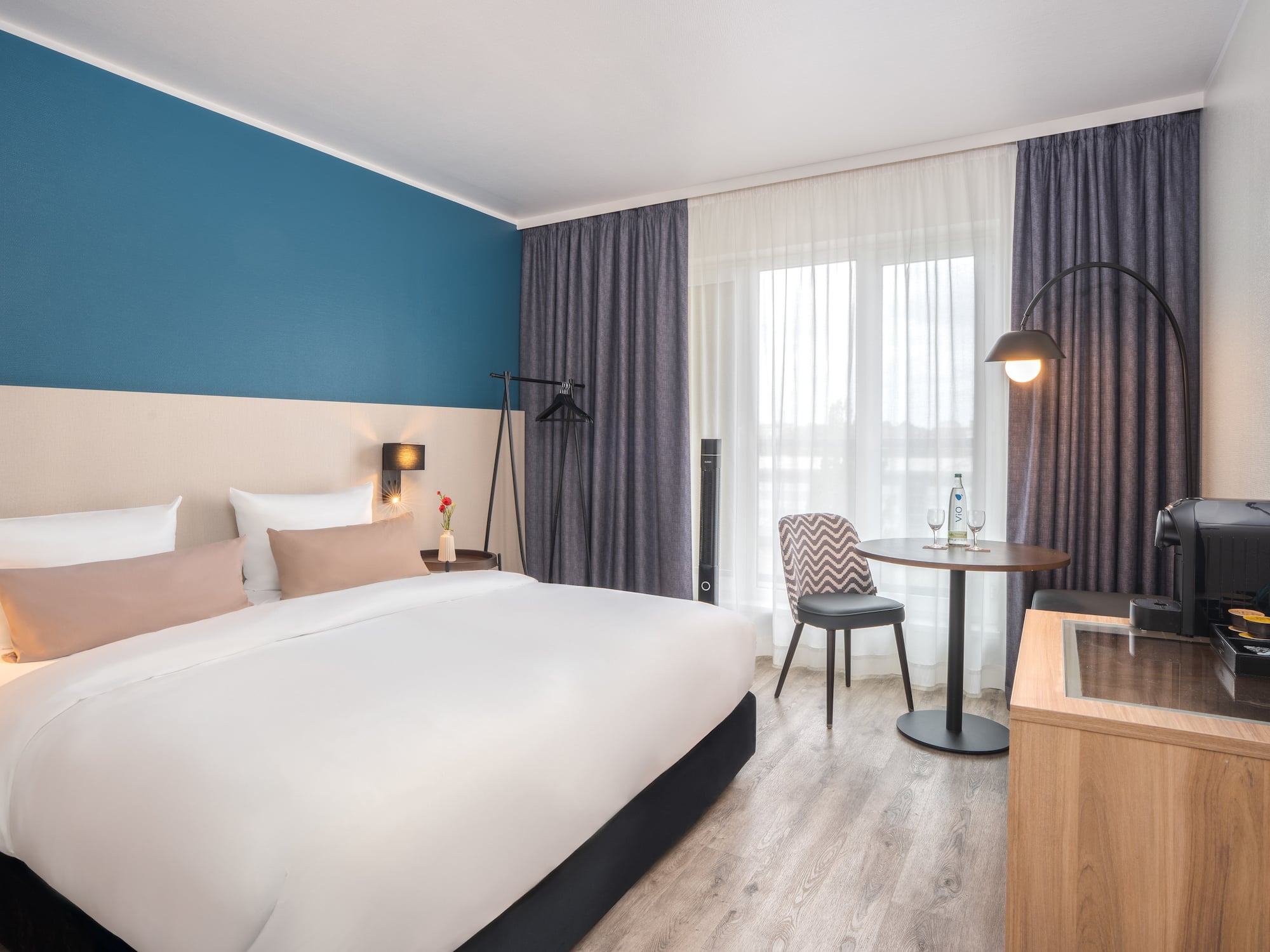 Modern hotel room interior with comfortable bed, blue accent wall, and table.