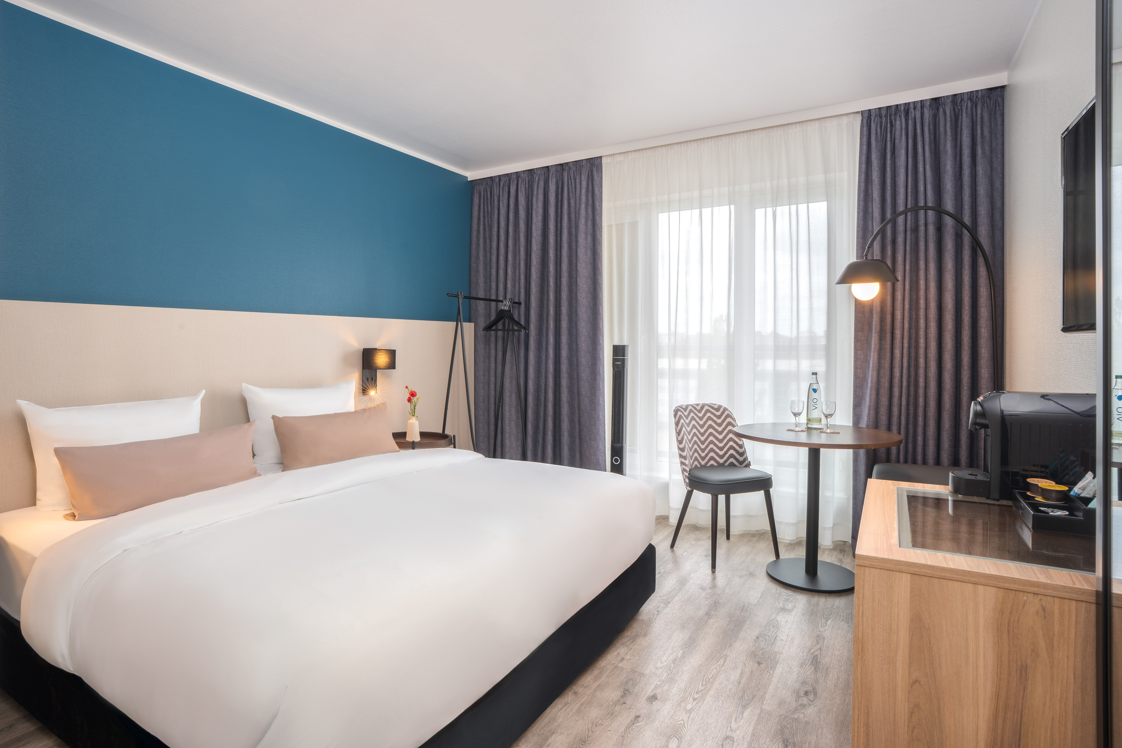 Modern hotel room interior with comfortable bed, blue accent wall, and table.