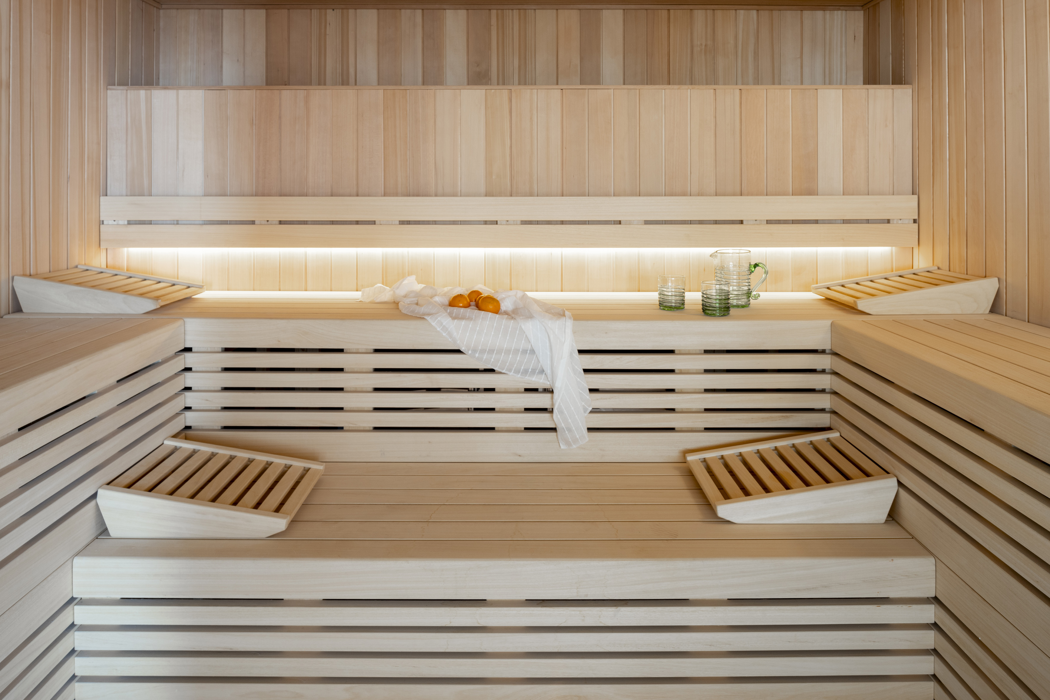 Modern light wood sauna with benches, soft backlighting, oranges, and glasses.