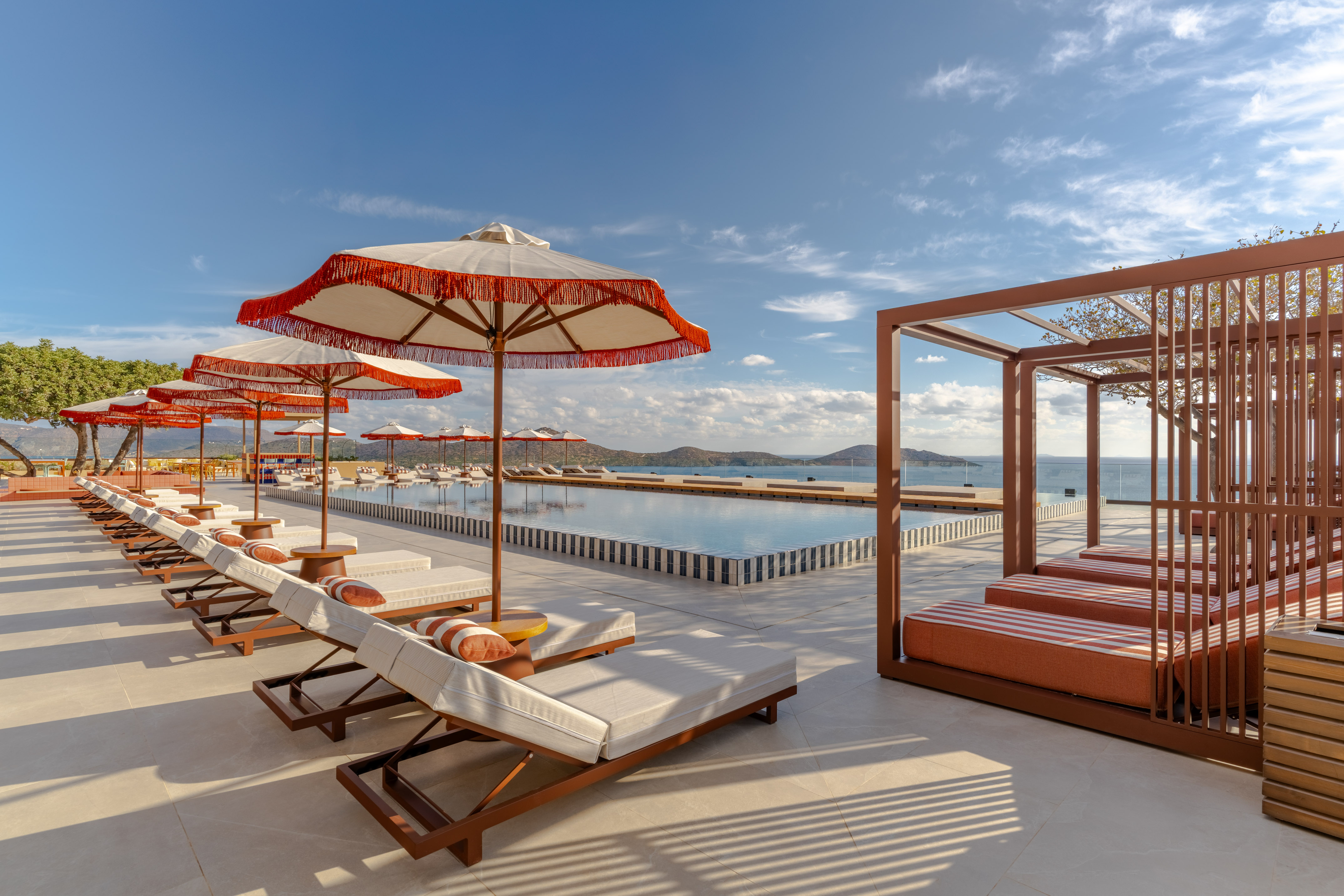 Luxury resort infinity pool, ocean view, sunbeds, and red umbrellas.