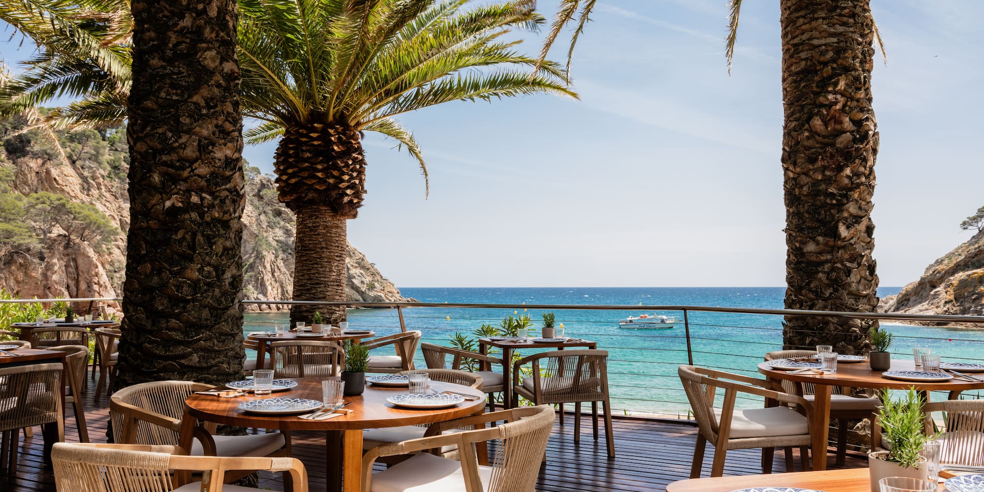 a table and chairs on a deck with palm trees and a body of water