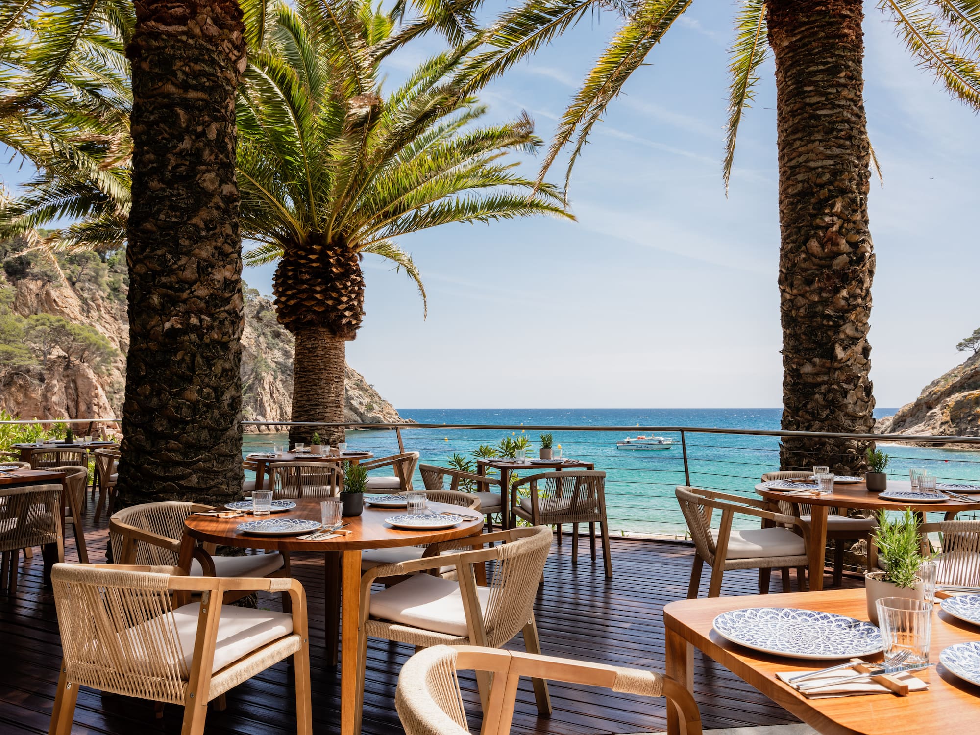 a table and chairs on a deck with palm trees and a body of water