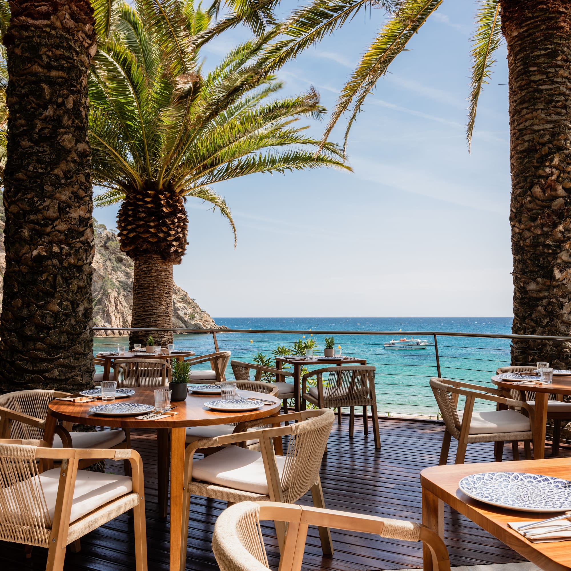 a table and chairs on a deck with palm trees and a body of water