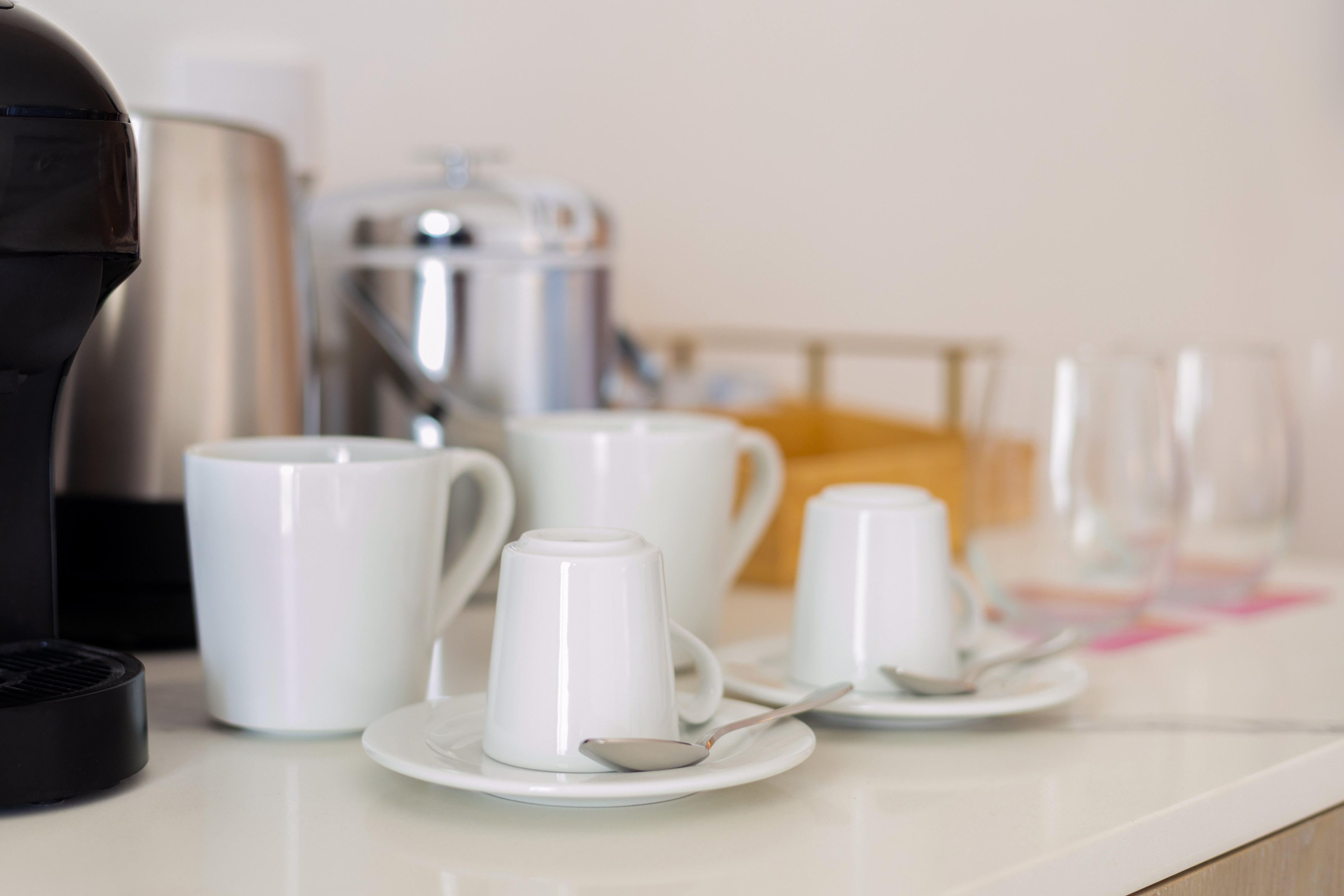 Beverage station with coffee maker, electric kettle, and white cups on counter.