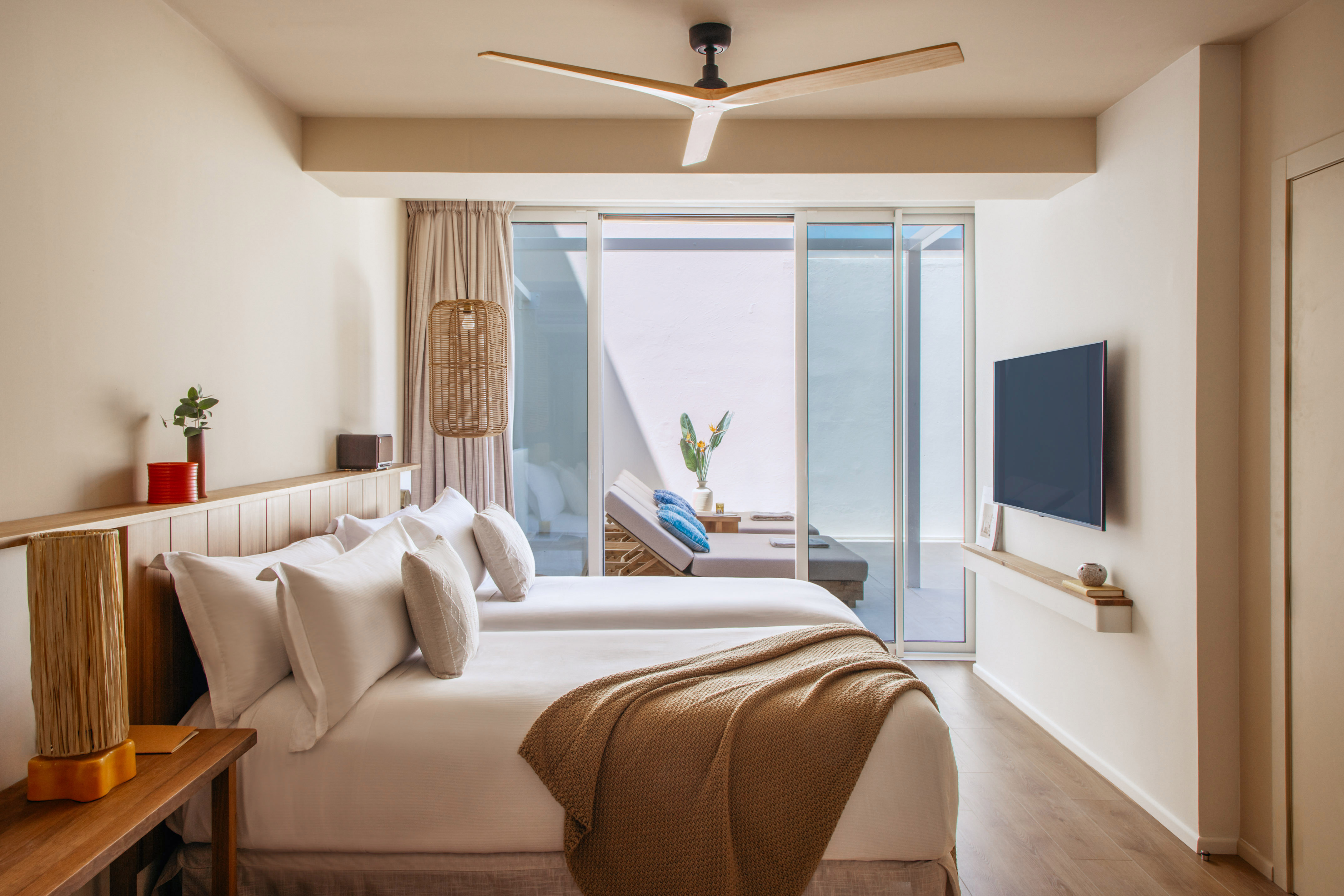 Modern hotel bedroom with two beds, private patio, ceiling fan, and TV.
