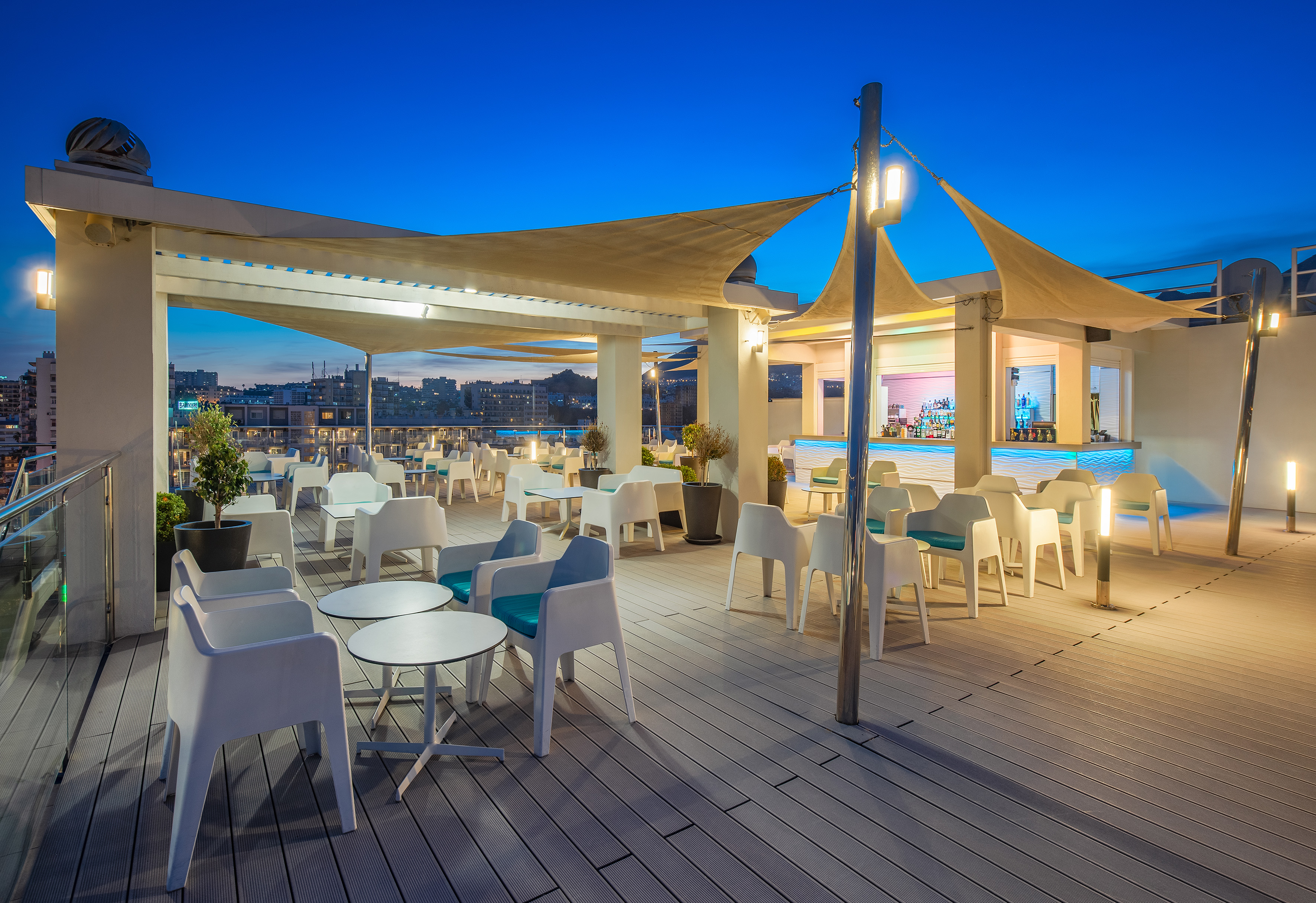 Rooftop bar lounge with modern seating, canopies, and city view at night.