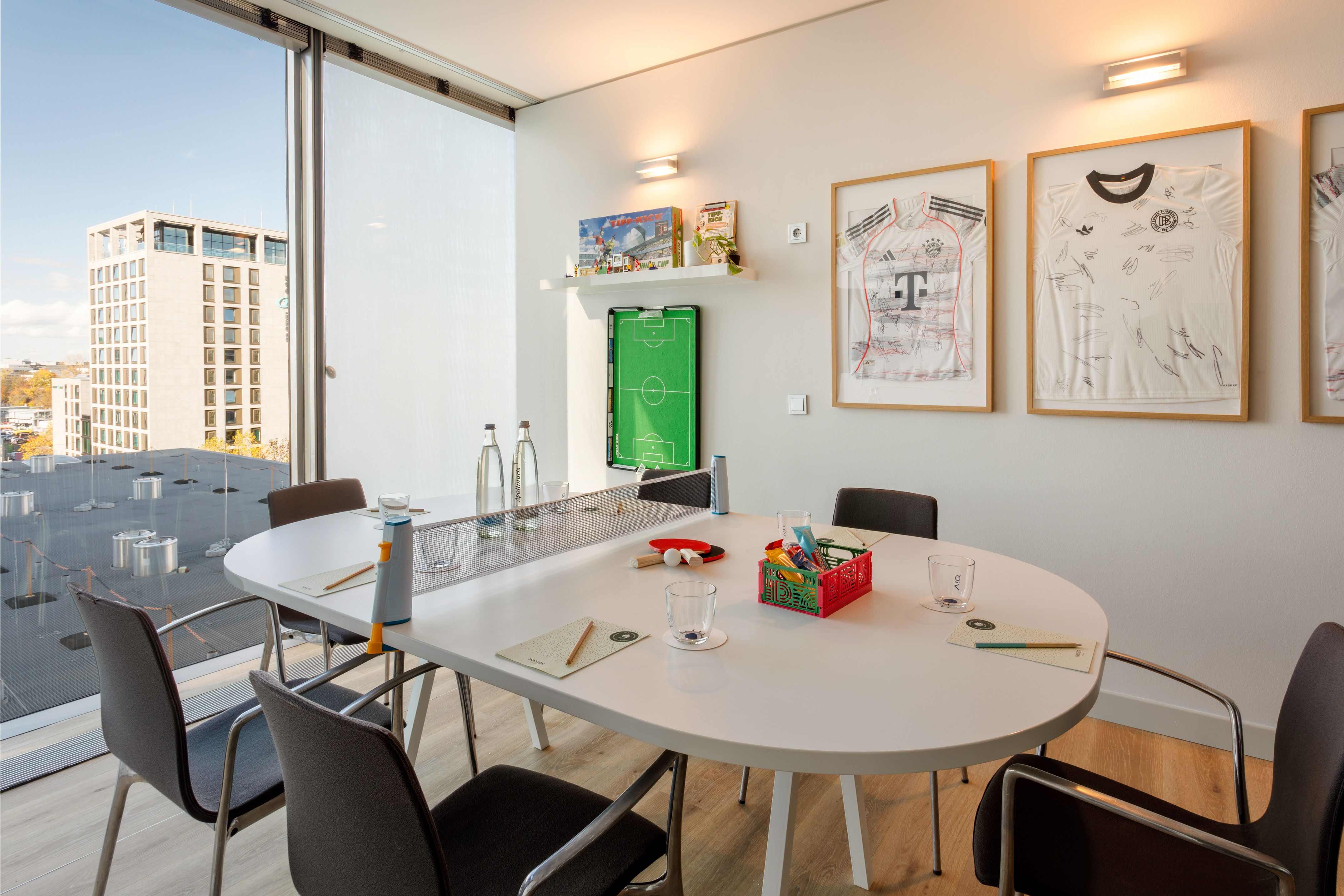 Modern conference room with oval table, city view, soccer decor, and ping-pong net.