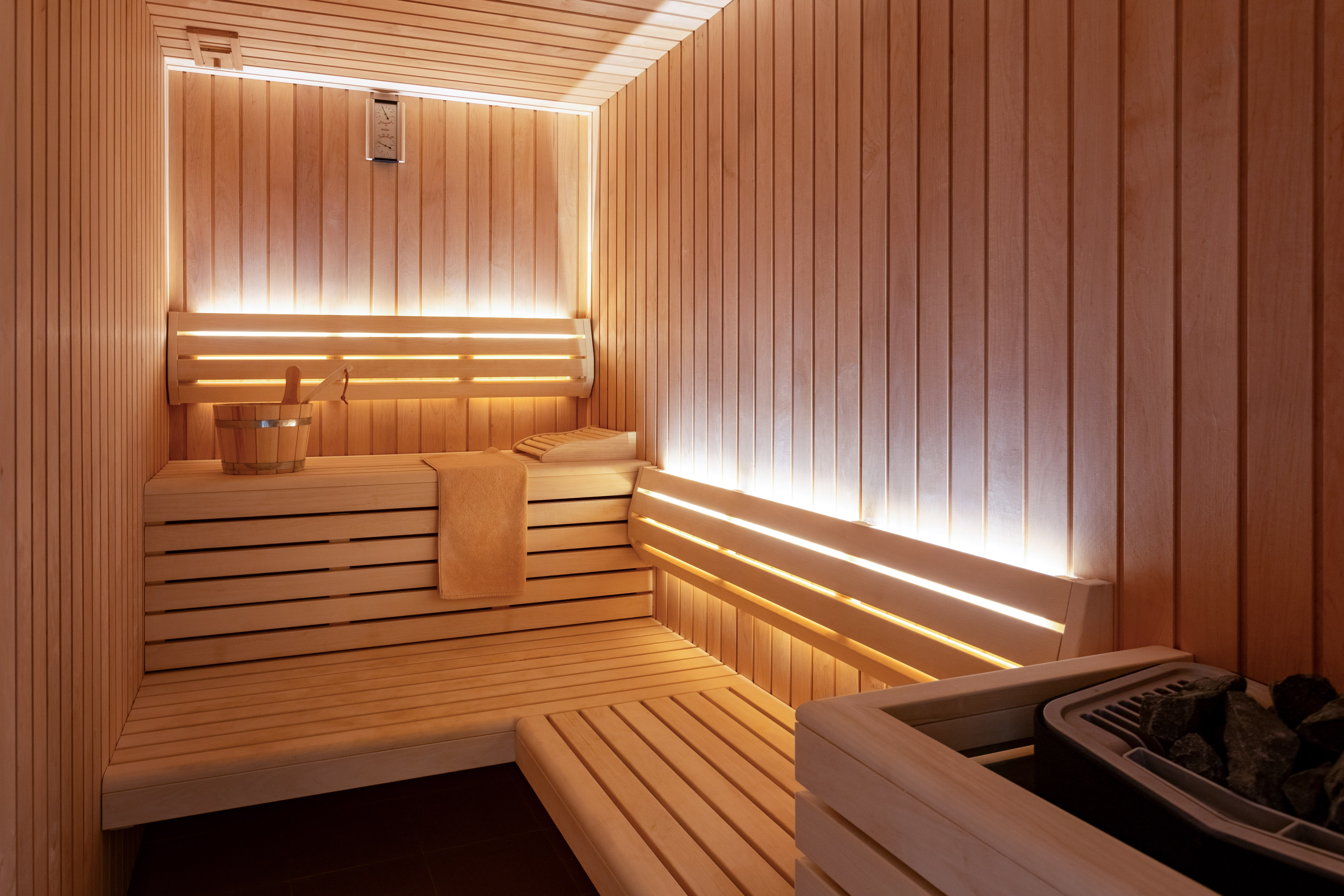 Light wood sauna with warm indirect lighting, benches, and heater.