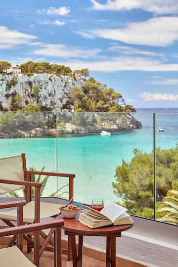a table with a bowl of fruit and a book on it with a view of the ocean and a cliff