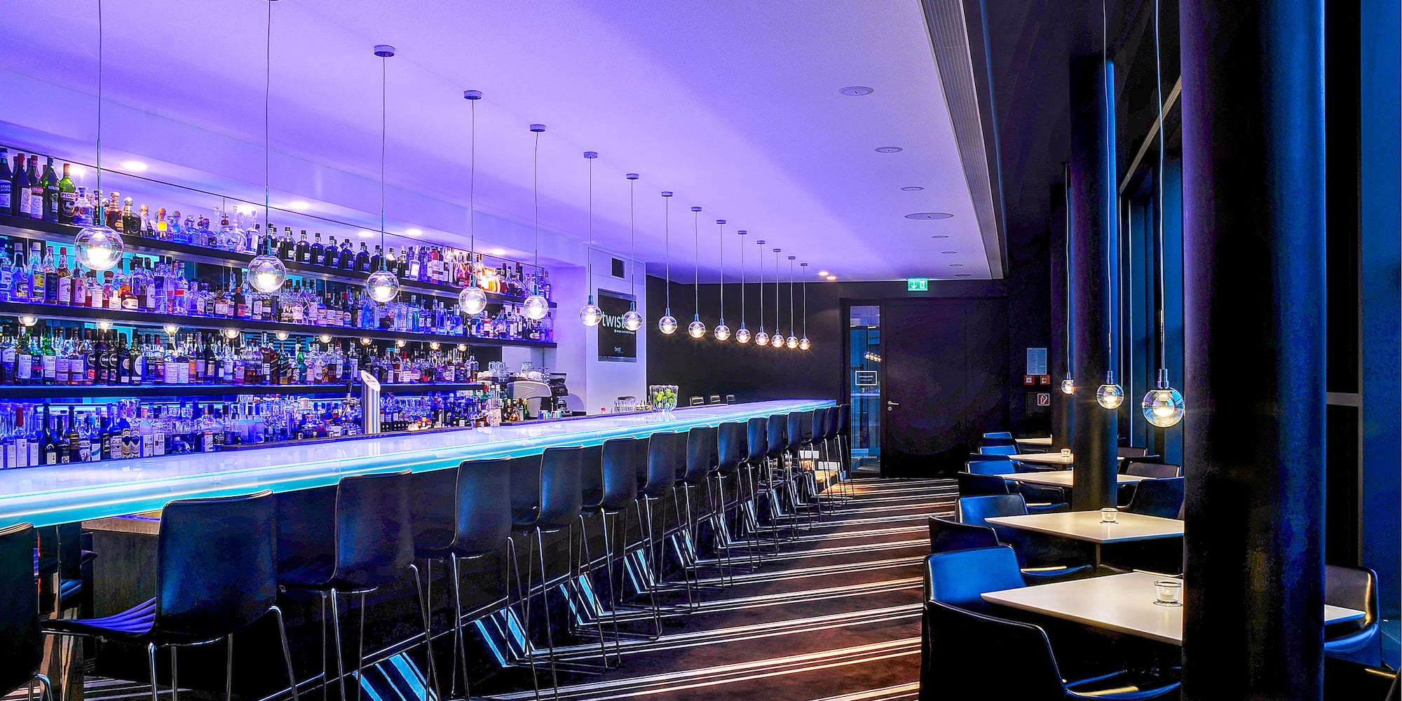 Modern bar lounge, blue lighting, long counter, liquor bottles, bar stools. - Twist Bar - INNSiDE Dresden, Dresda