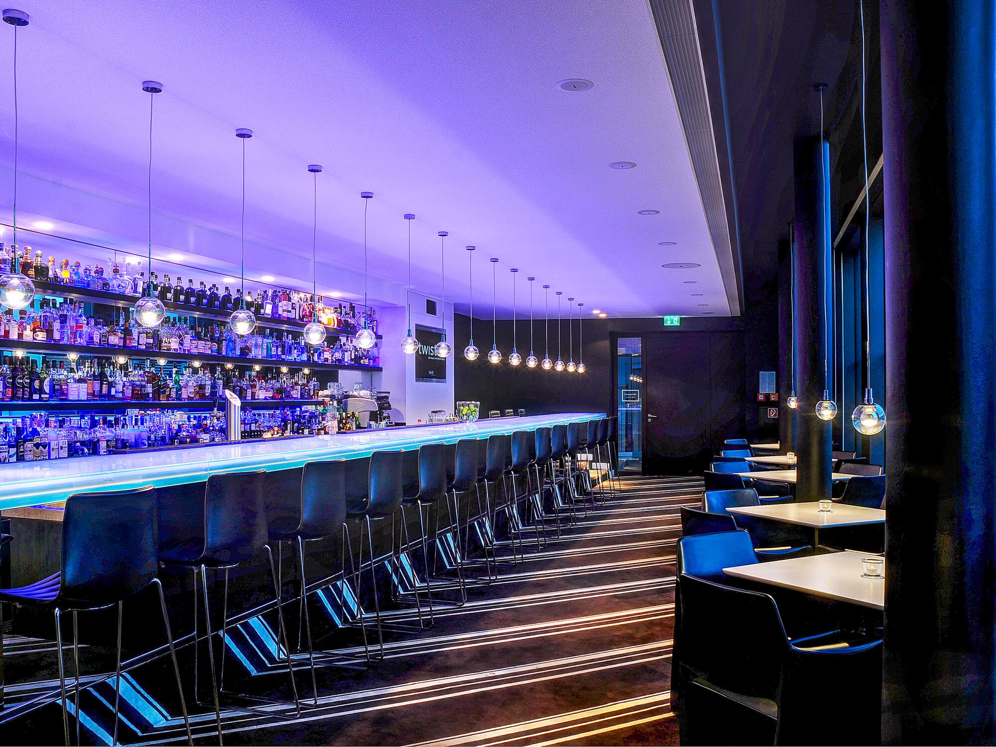 Modern bar lounge with blue illuminated counter, purple lighting, and bottle shelves. - Twist Bar - Innside Dresden, Drážďany