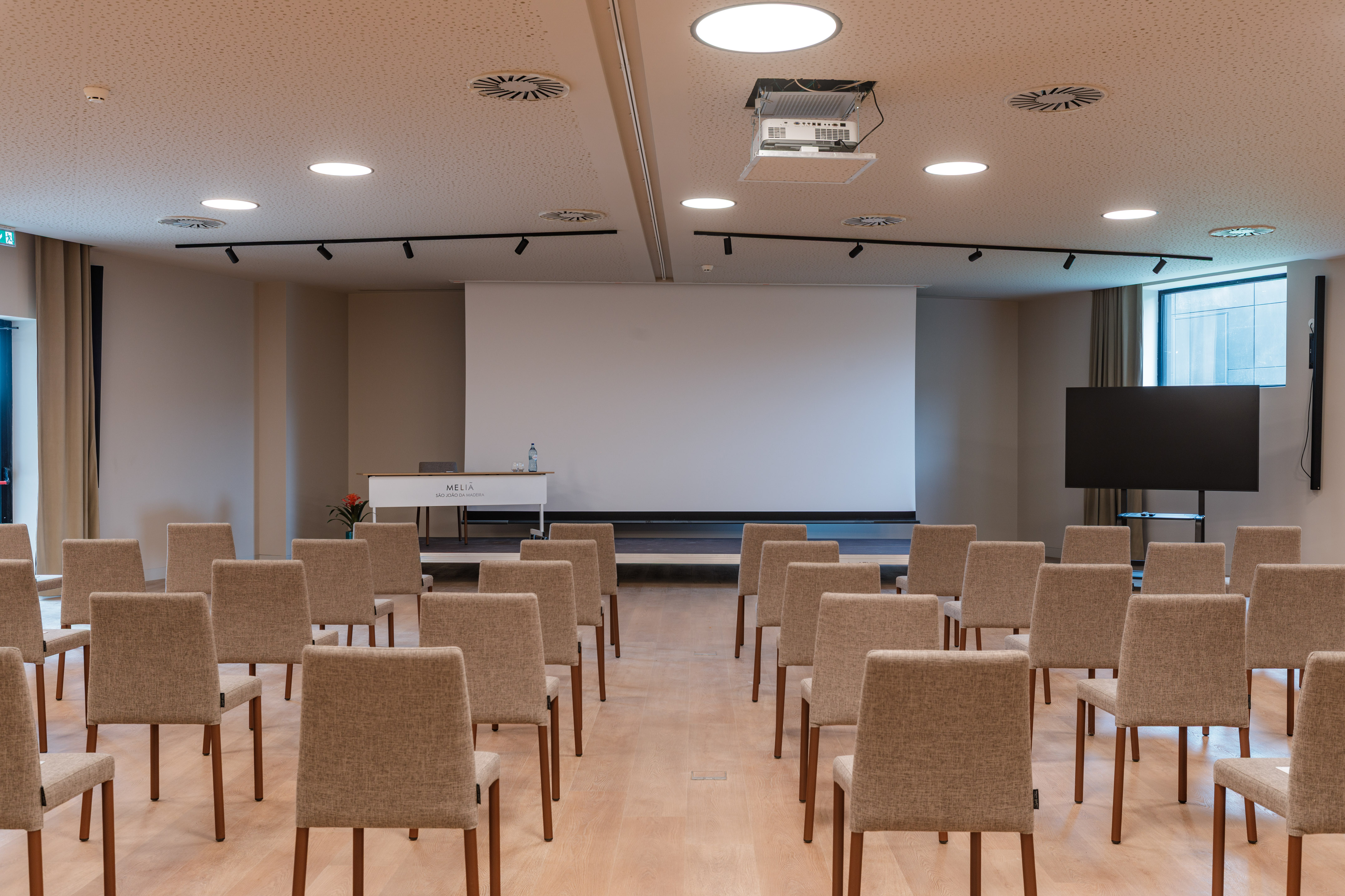 Modern meeting room setup with rows of chairs, projector, screen, and TV.