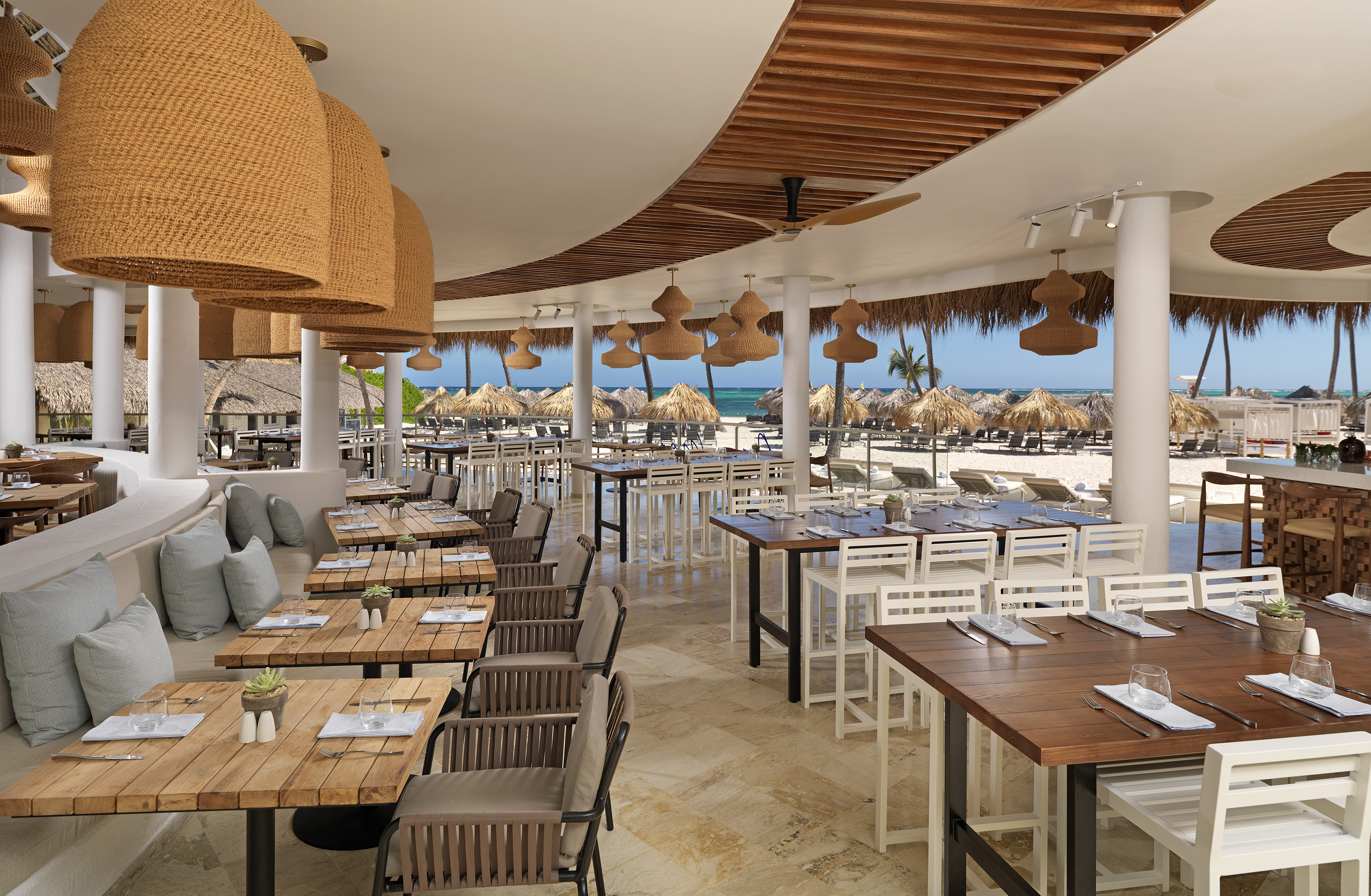 Beachfront restaurant with outdoor tables, woven lights, and ocean view.