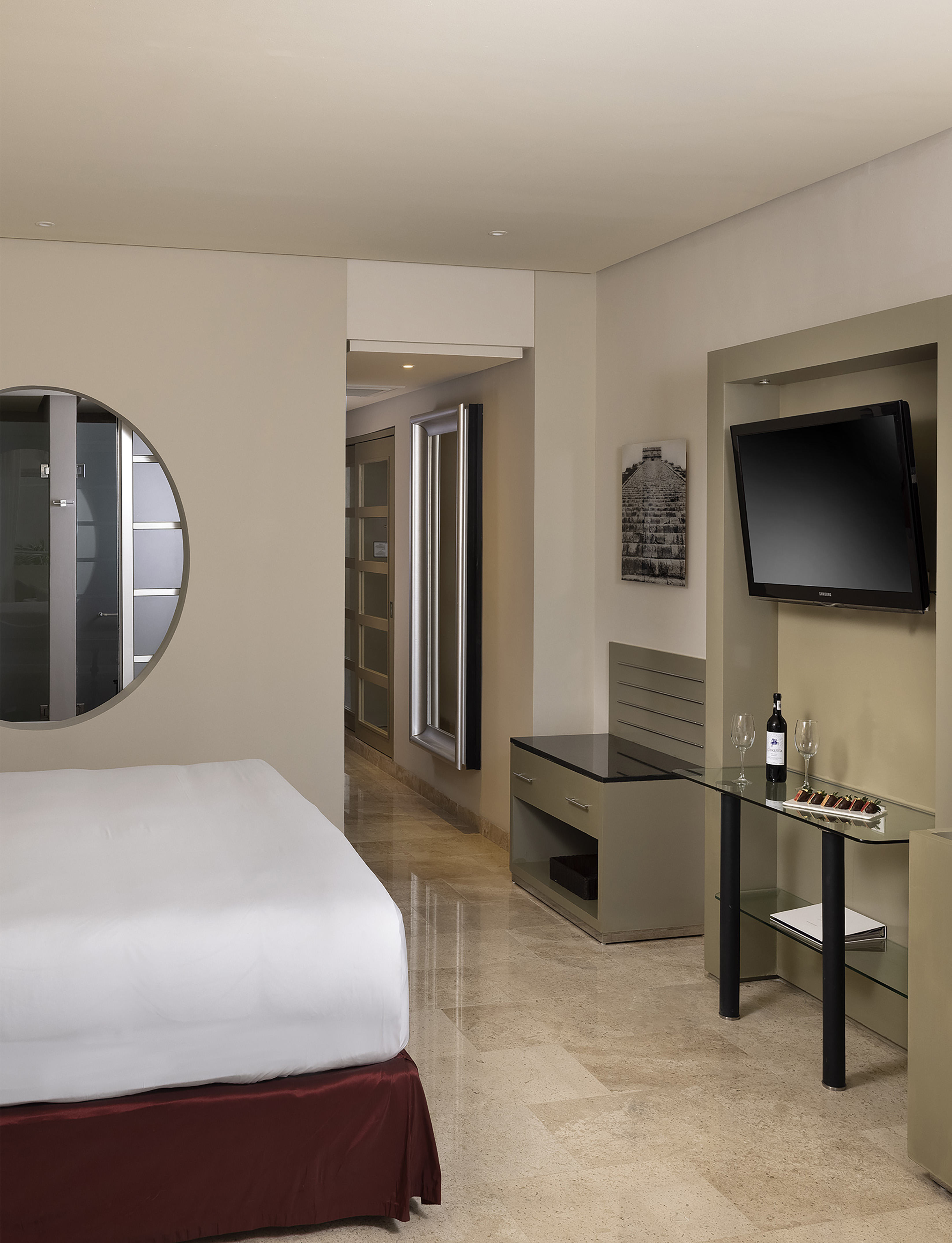 Modern hotel room with bed, TV, wine, and chocolates on a glass table.